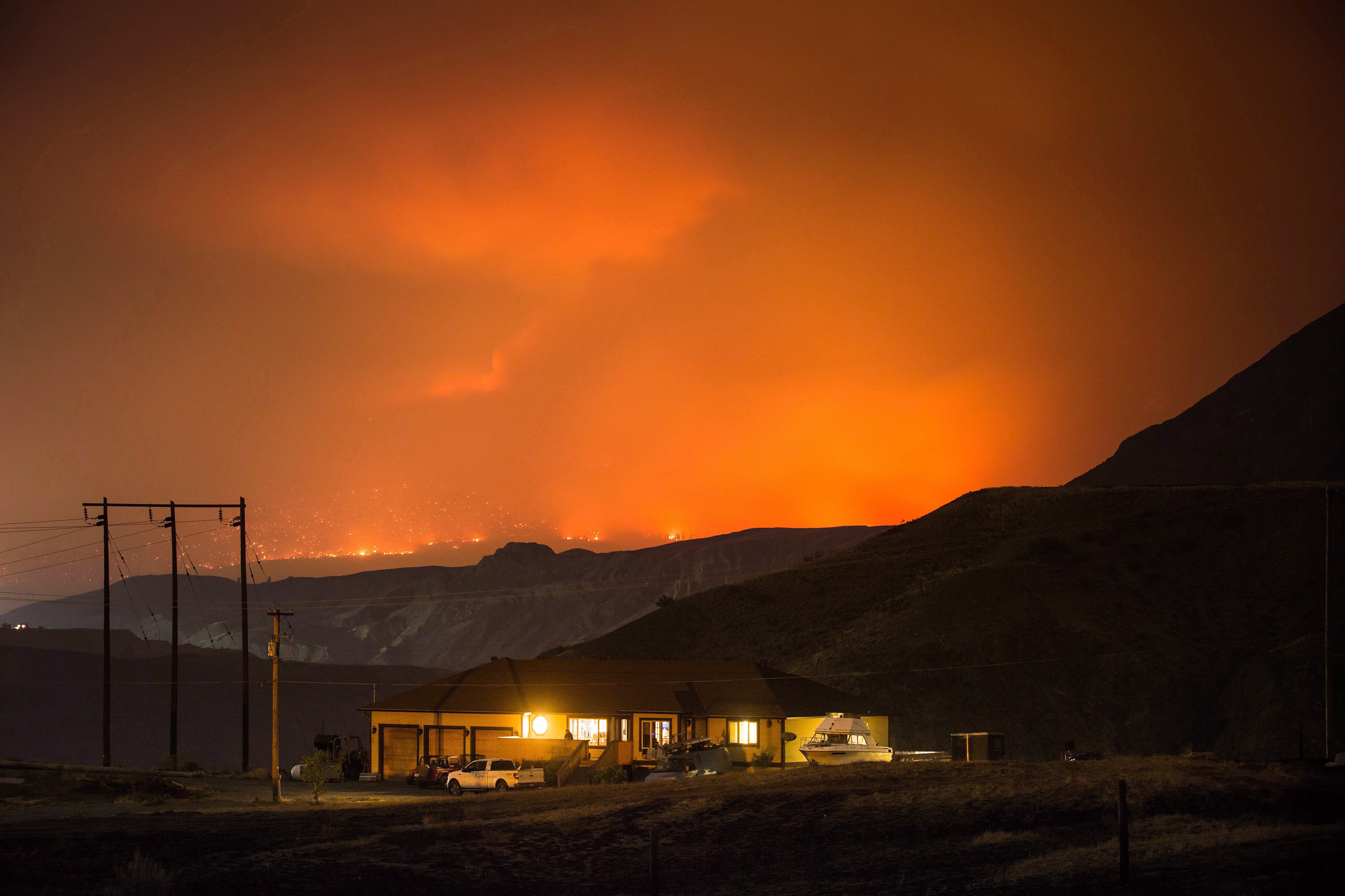 A wildfire burns on a mountain in the distance east of Cache Creek behind a house in Boston Flats, B.C., in the early morning hours of July 10, 2017. (Darryl Dyck/The Canadian Press)