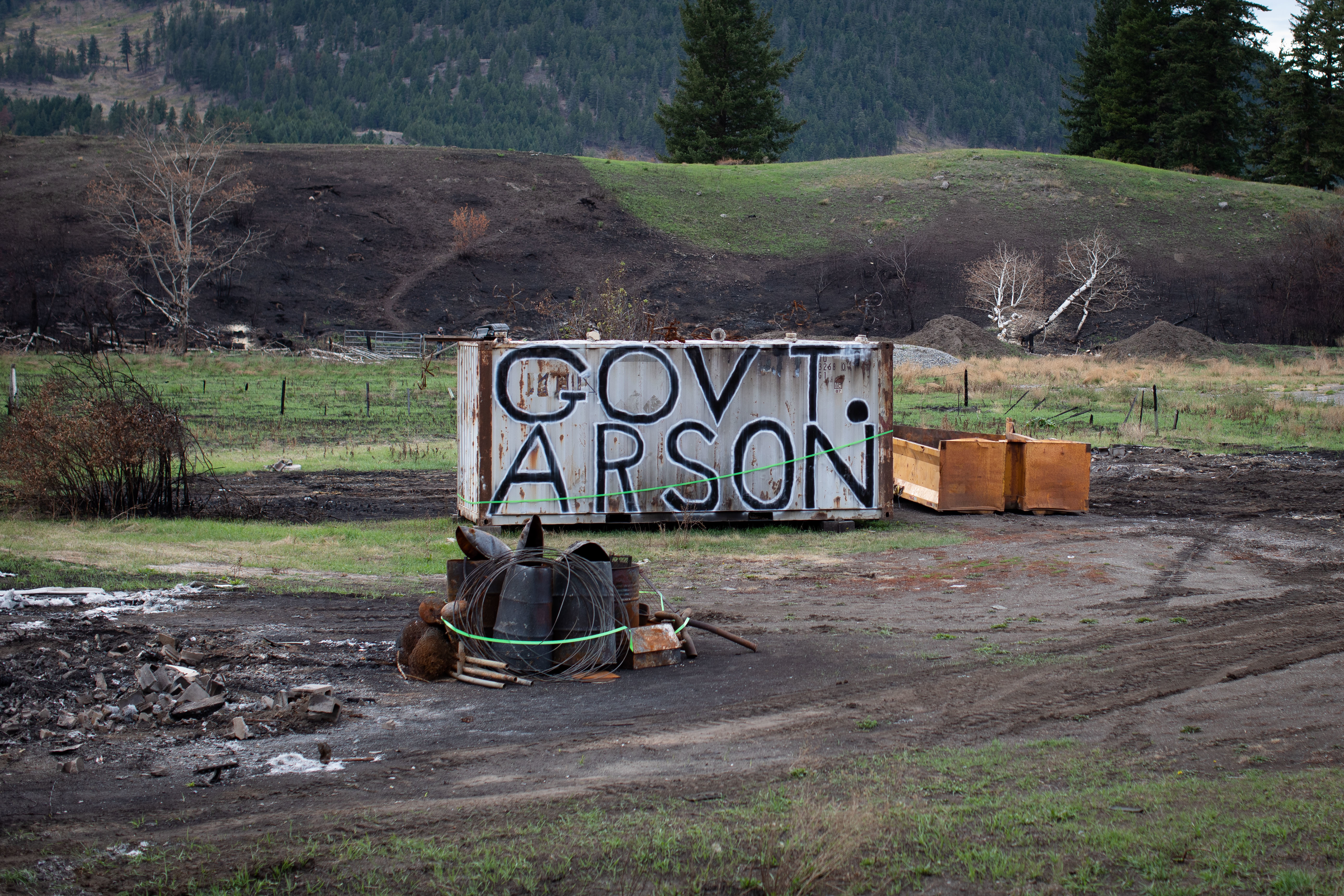 An anti-government message is written on the side of a shipping container near the remnants of a burned-down trailer home in Monte Lake, B.C., on Sept. 1. (Maggie MacPherson/CBC)