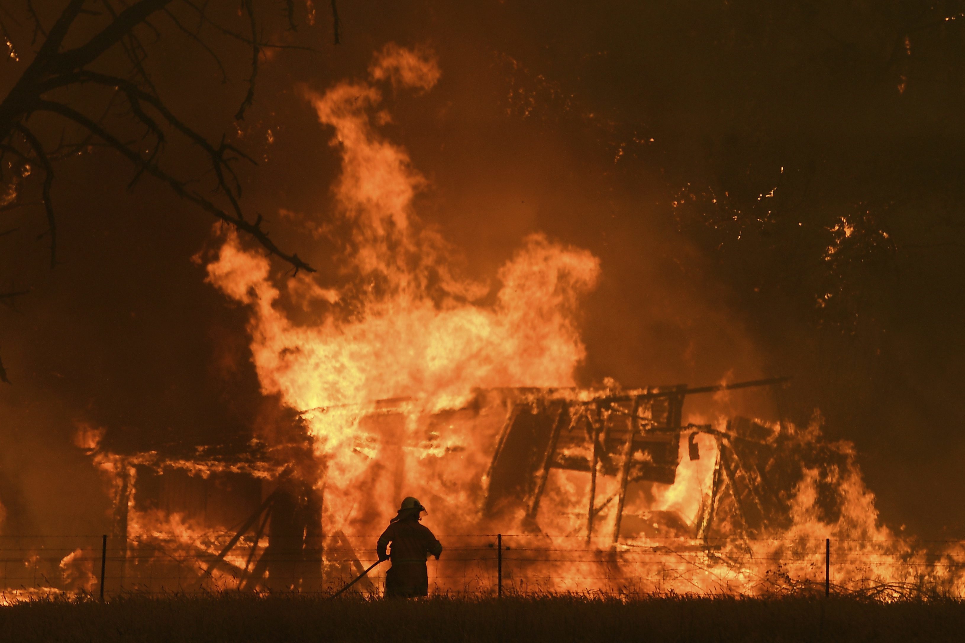 In this Saturday, Dec. 21, 2019, photo, NSW Rural Fire Service crews fight the Gospers Mountain Fire as it burns a structure at Bilpin. Deadly bushfires raged across several states, destroying homes and claiming the lives of two volunteer firefighters. (Dan Himbrechts/AAP Images)