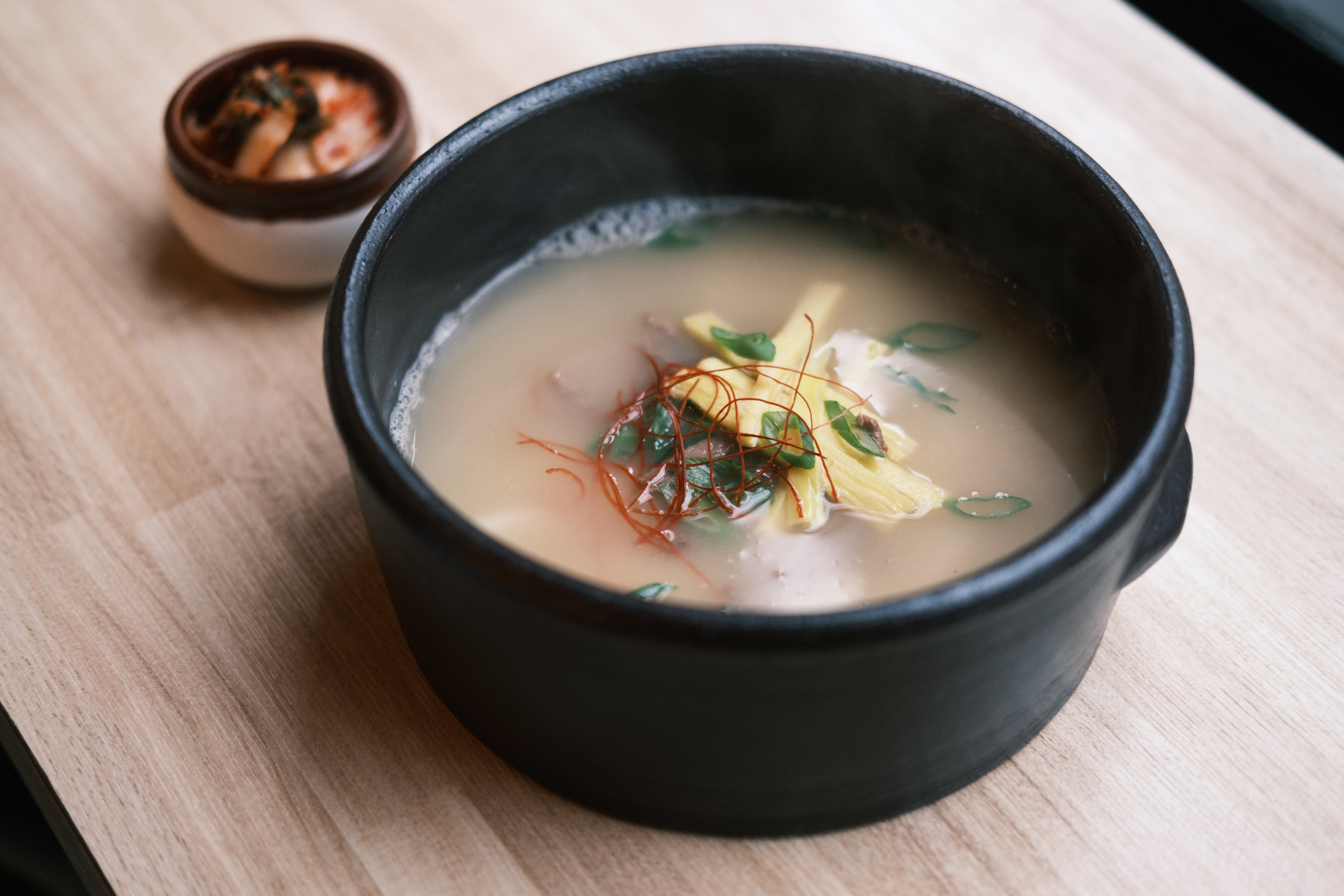 Dduk guk, a rice cake soup with shredded beef, sliced egg and a side of kimchi at Millsam Tacorea in Vancouver.