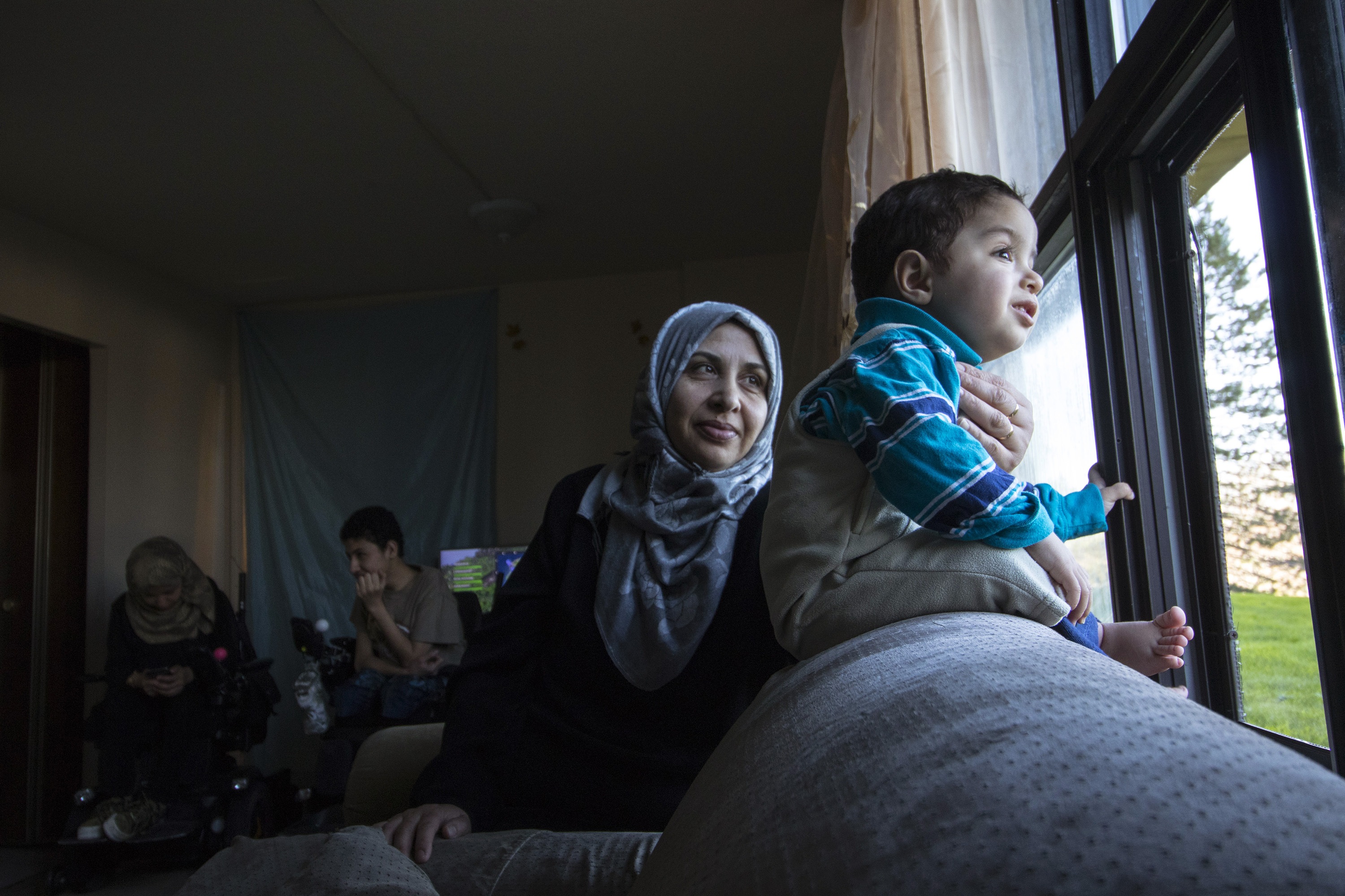 Eighteen-month-old Mias looks out the window of the family's apartment as his mother, Jawaher Aljanadi, looks on. Maher and Marwa are in the background. (Dave Irish/CBC)