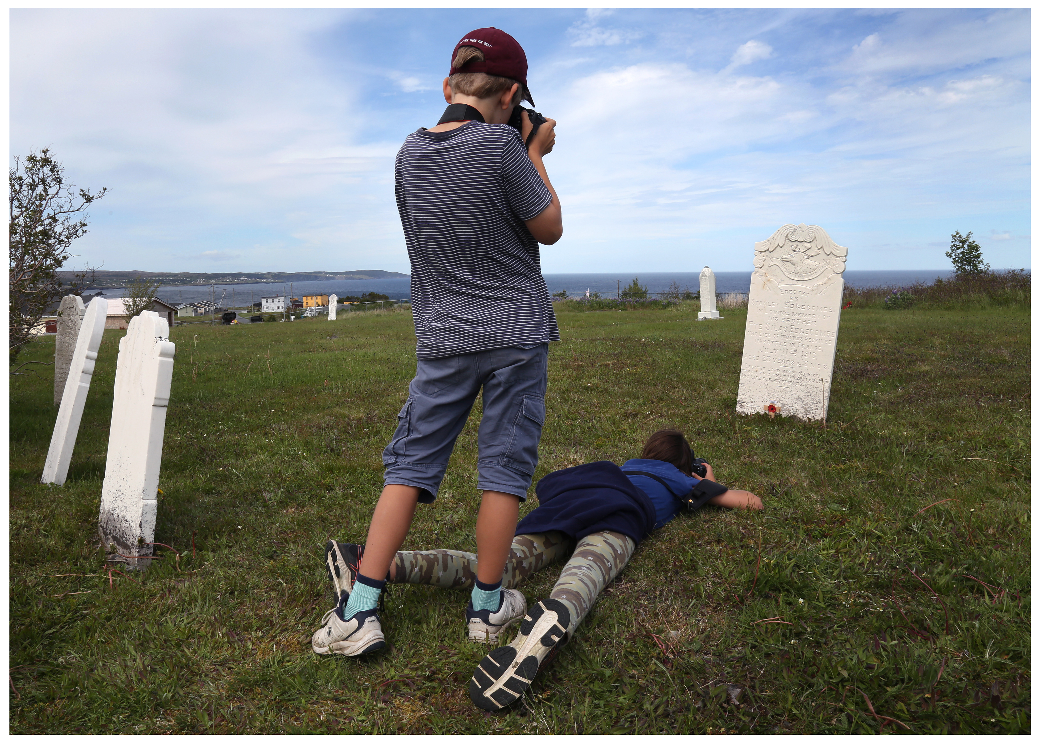 Students Oscar Heard, standing, and Zoe Spenceley, photograph the memorial marker for Silas Edgecombe, which his brother built at Ochre Pit Cove. (Paul Daly for CBC)