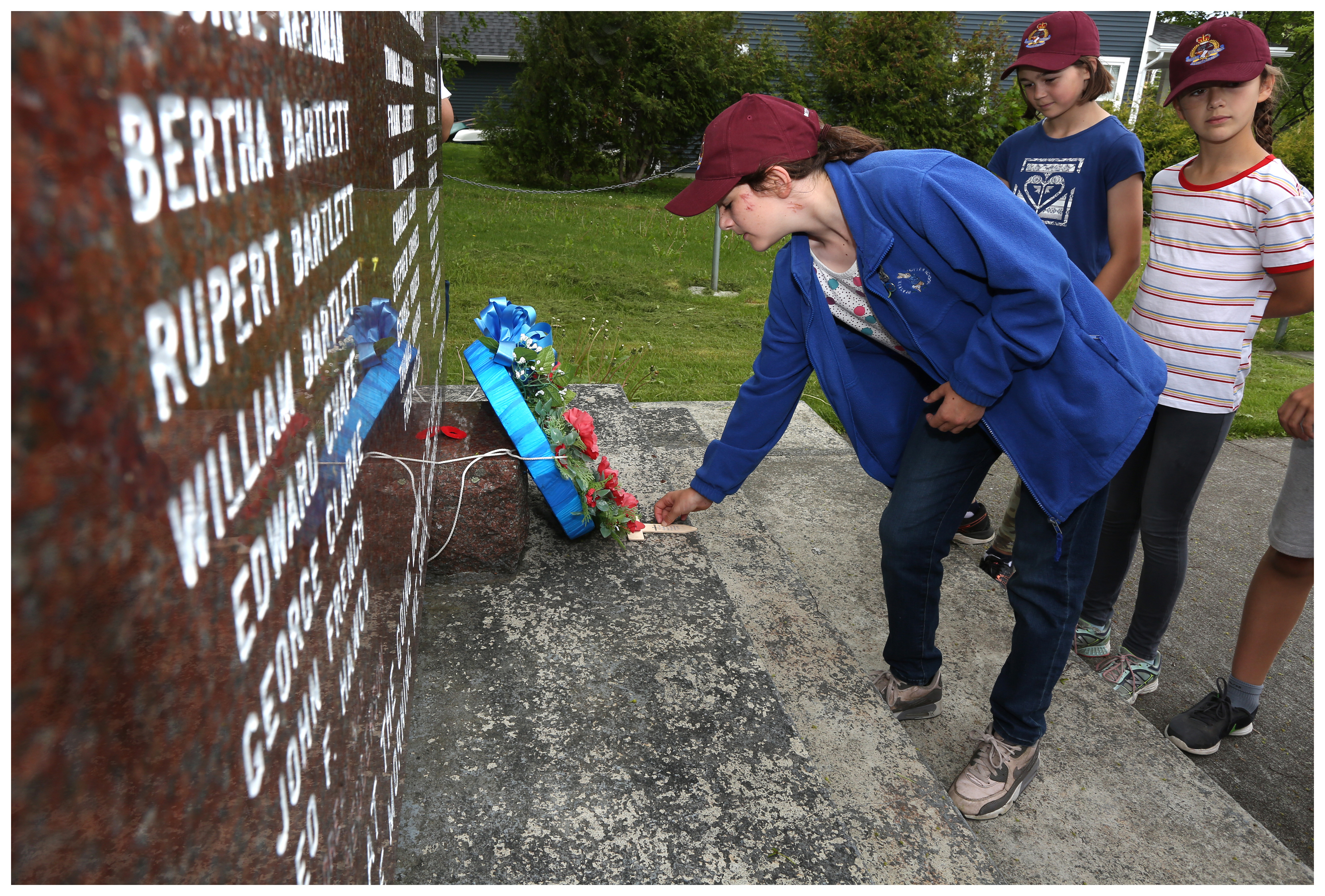 Alice Goldberger, observed by Zoe Spenceley (left) and Sophia Anderson, leaves a cross they made for nurse Bertha Barrett at the War Memorial in Bartlett's hometown of Brigus. (Paul Daly for CBC)