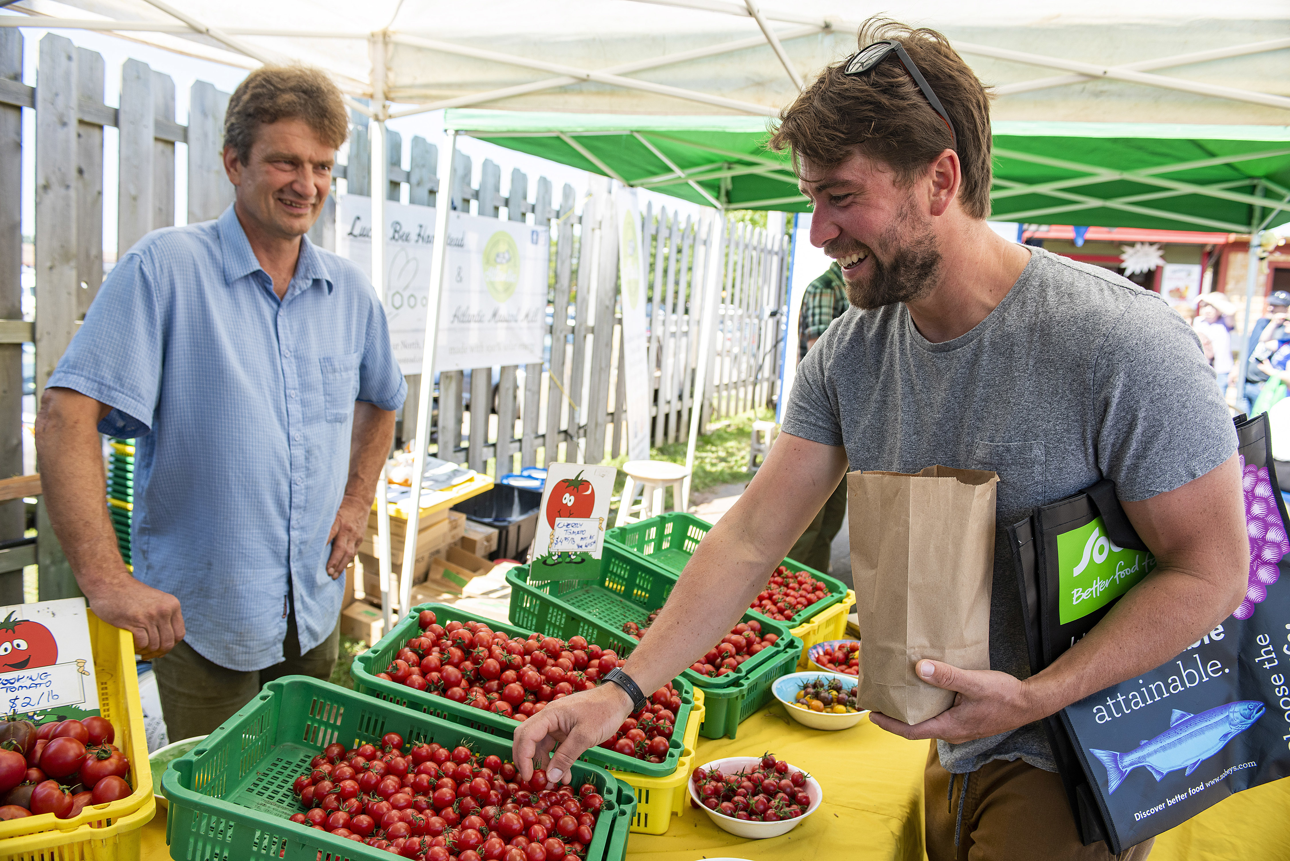 Colin Hughes, left, of Calydon Farms in Lower Montague, chats with Joseph Crawford, on vacation from Calgary, Alta., as he buys some cherry tomatoes at Hughes’s booth at the Charlottetown Farmers Market recently. Brian McInnis/CBC