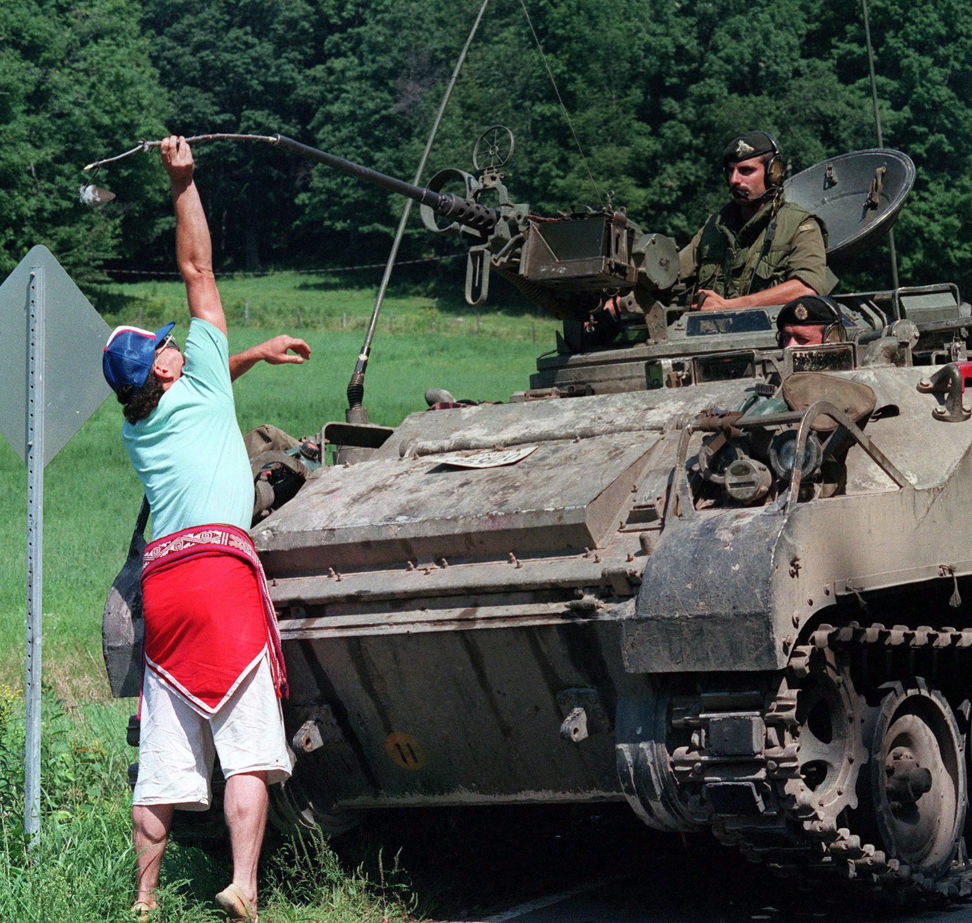 A man places a stick with an eagle feather tied to it into the barrel of a machine gun mounted on an army armoured vehicle at Oka, Aug. 23, 1990. (Bill Grimshaw/Canadian Press) 