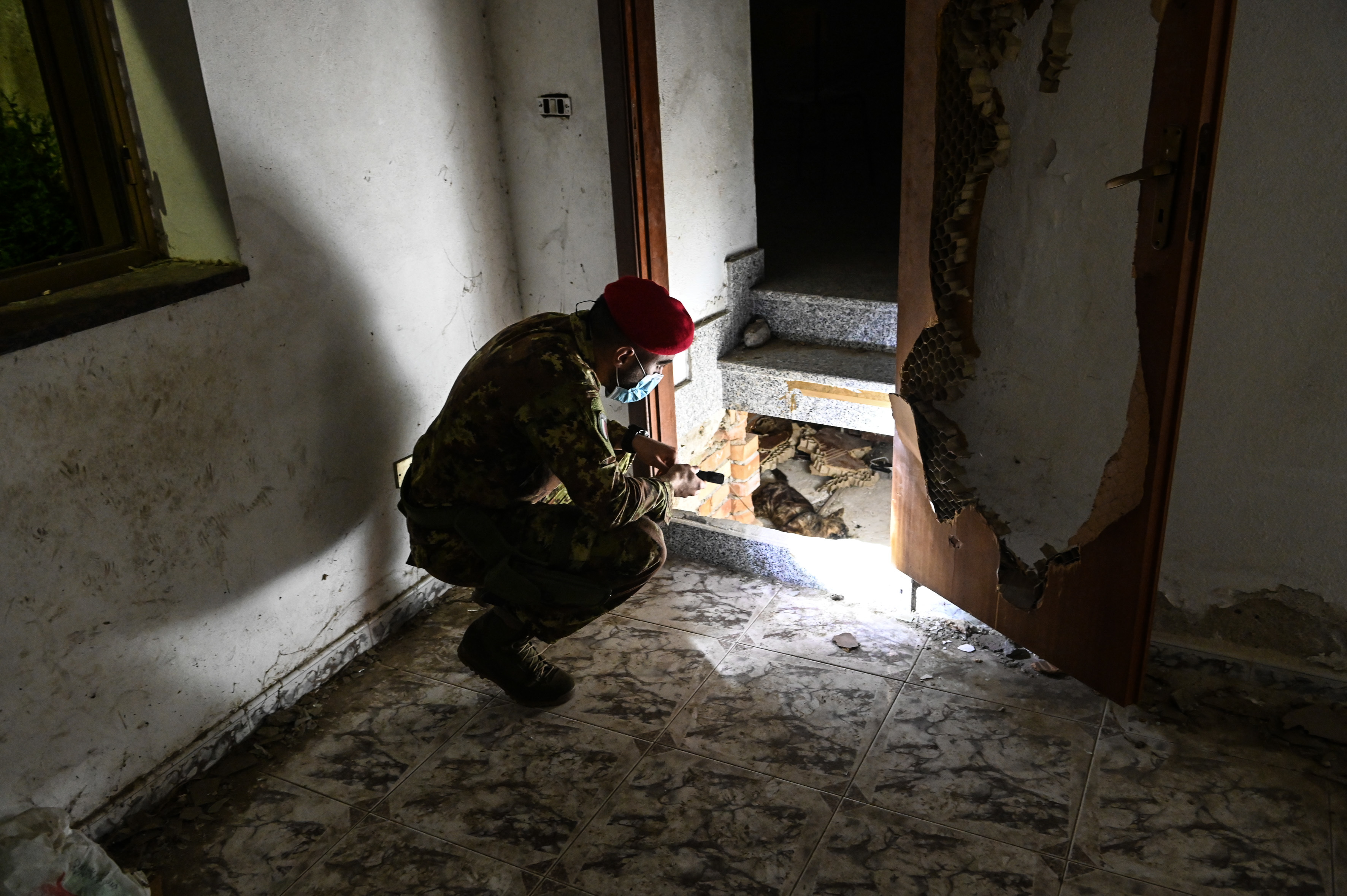 A Cacciatore officer shines a flashlight on a dead cat someone has laid across the entrance to a  hidden bunker discovered in a police raid years ago, a sign, he says, of the town’s displeasure at journalists visiting. (Chris Warde-Jones)