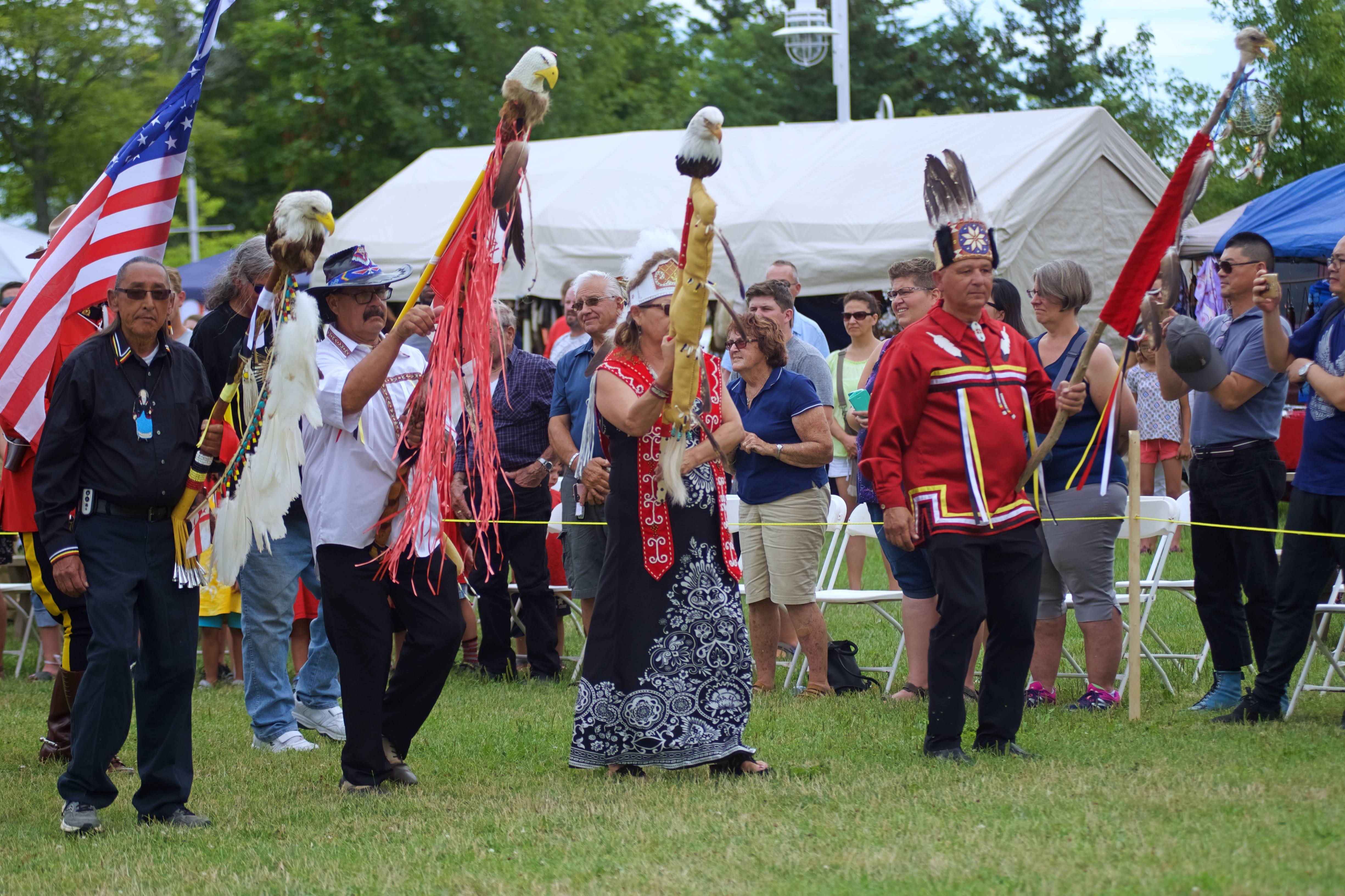 Grand entry is done at start time each day, with leaders and dancers entering through the east side of the grounds. The chiefs will lead, and will often carry staffs, or be accompanied by staff carriers. These staffs are sacred, given to chiefs, community leaders and elders within the community. After the staffs come the flags, followed by the dancers. Depending on the region or available flags, there will be the Mi’kmaw Nation Flag, the veteran flag, provincial flag, etc. The community will determine which flags will be used. Once all the flag carriers, and dancers enter the grounds, there will be a prayer by an elder. Next, a prayer for veterans and a special song will be played for veterans of all nations. (Patricia Bourque)