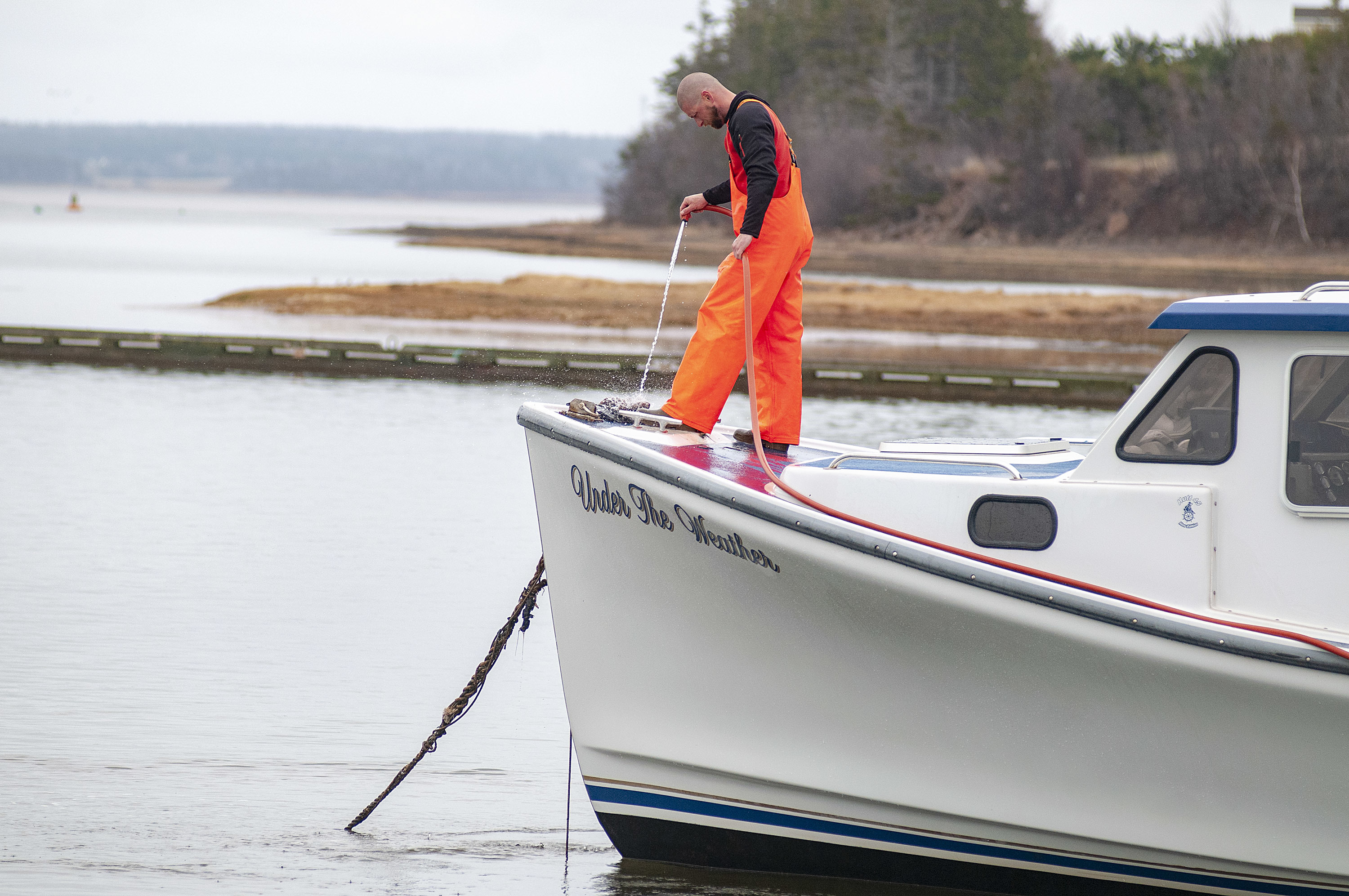 A crew member of Under the Weather hoses down the boat after a day of fishing. (Brian McInnis)