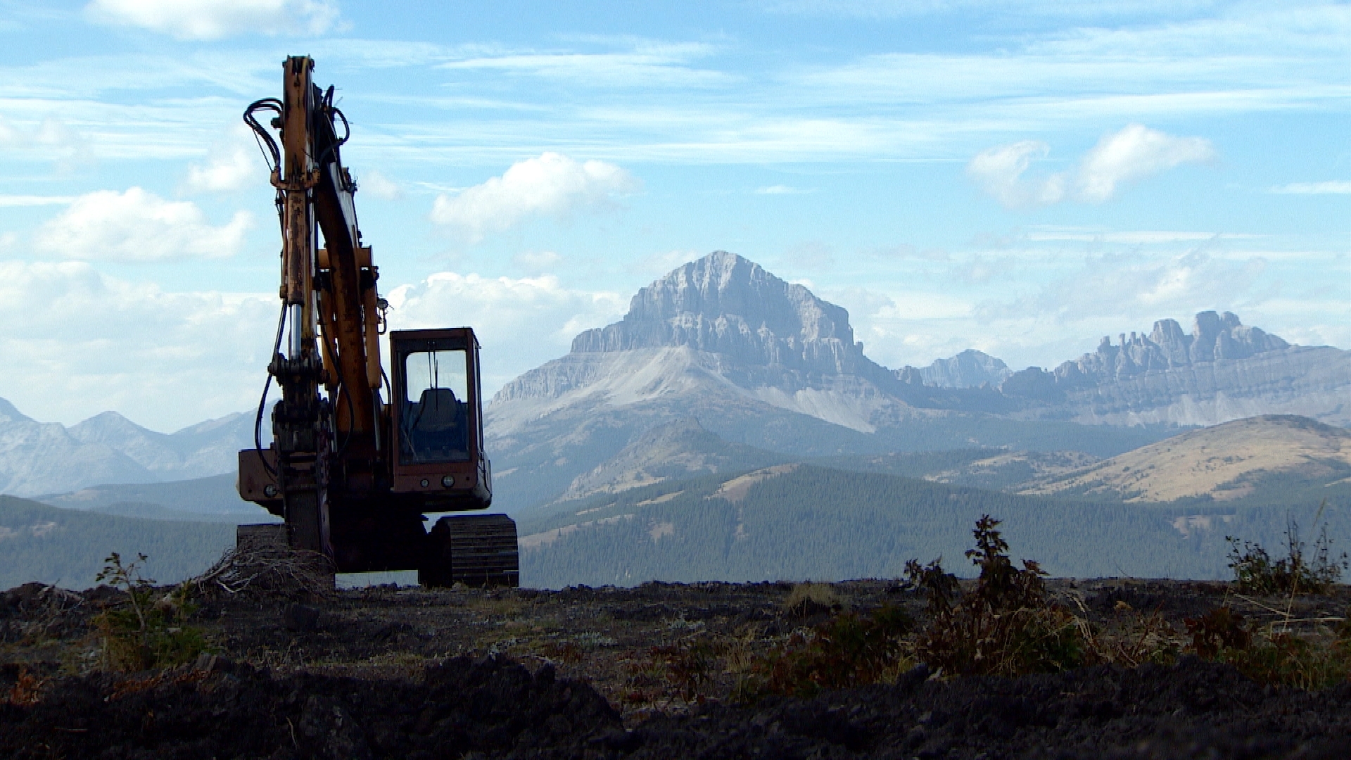 Construction equipment near Grassy Mountain in 2014, with the distinctive peak of Crowsnest Mountain in the background. (CBC)