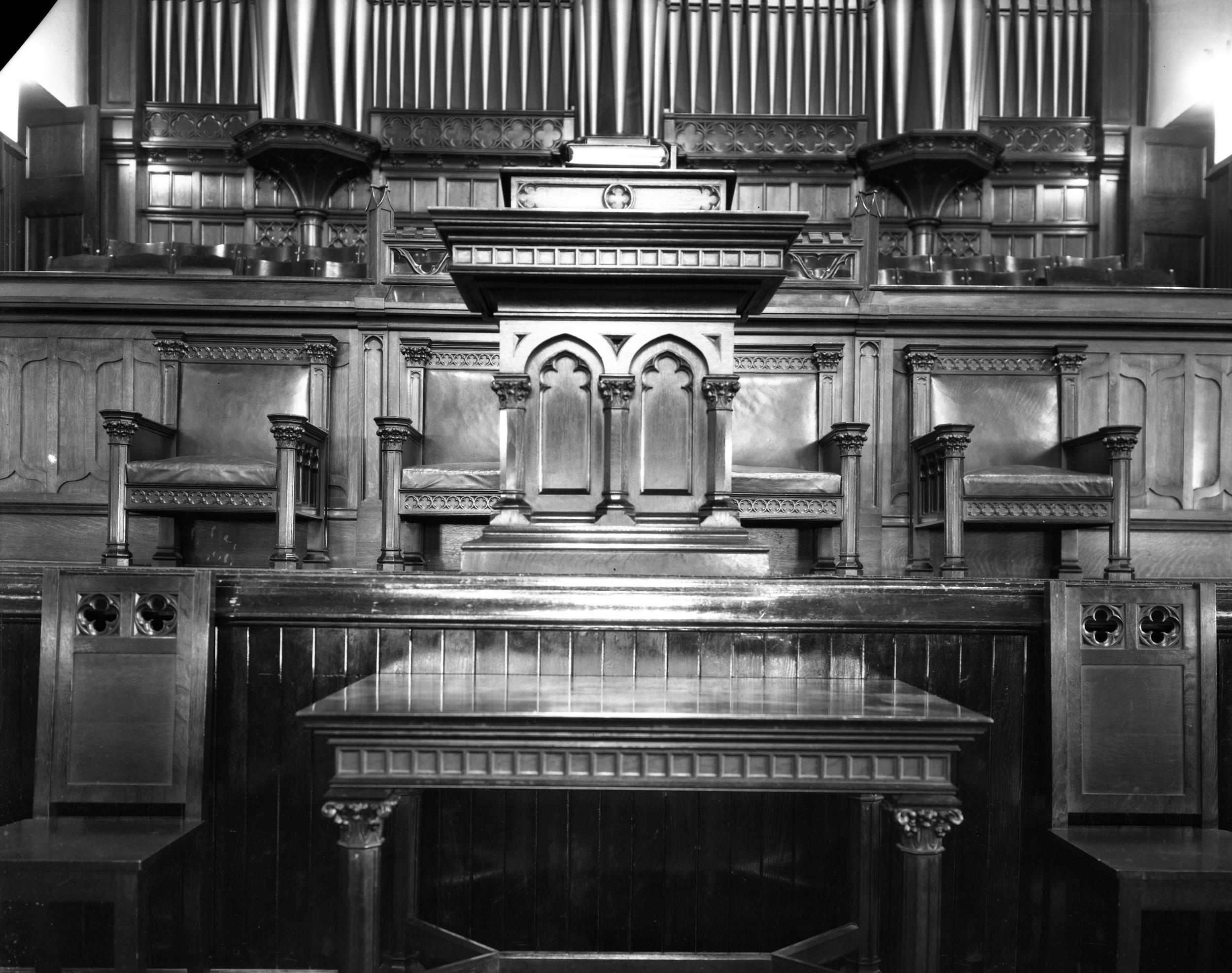 A photo, taken some time in the 1930s, of the church's interior looking towards the front, showing a close up of the communion table and pulpit with the organ and choir loft behind. (Saskatoon Public Library Local History Room. Picture ID: A-1667) 