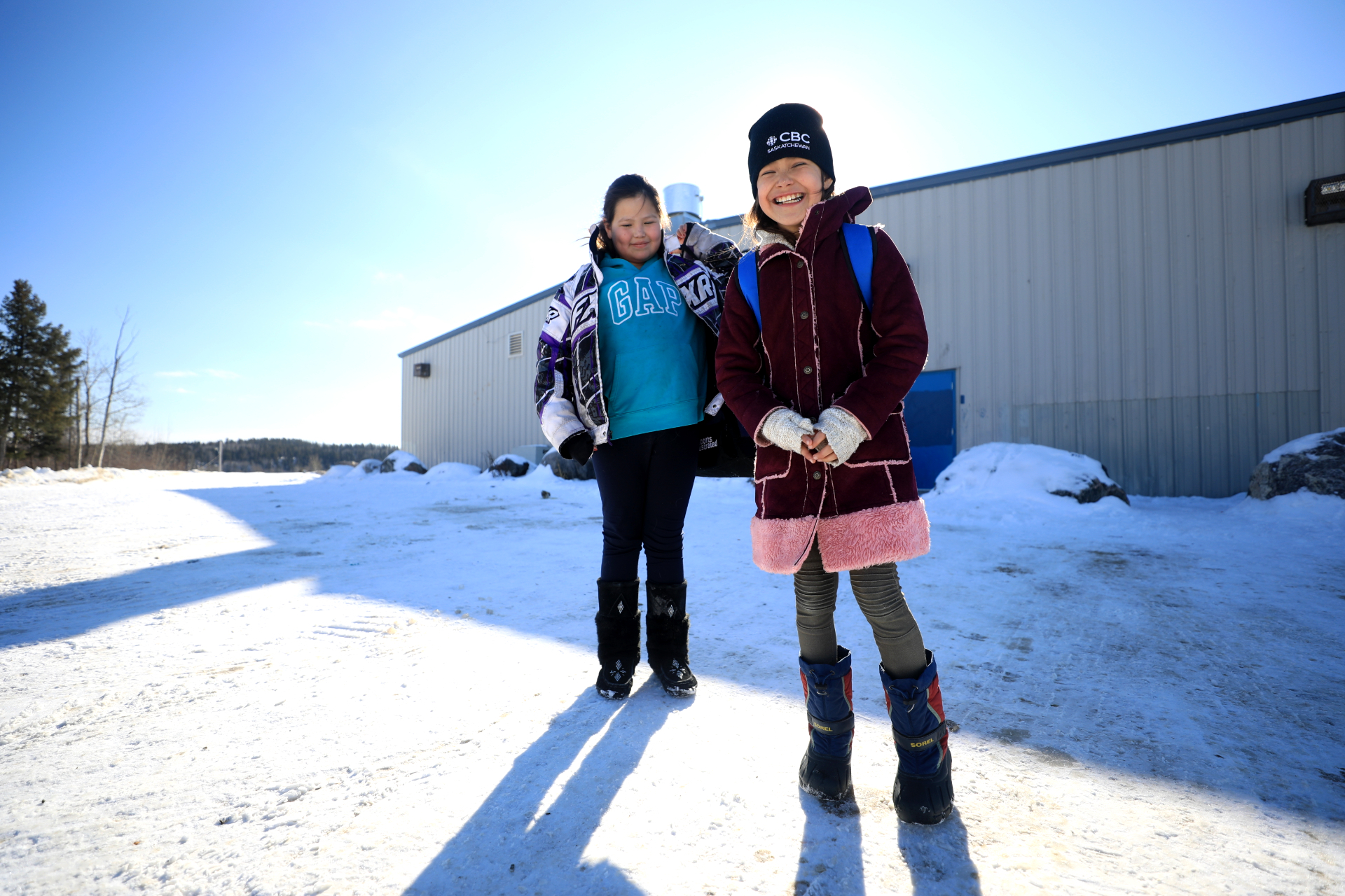 Two girls chat about the DSLR camera while waiting to go into the ice skating rink in Stanley Mission in March, 2020. (Heidi Atter/CBC)