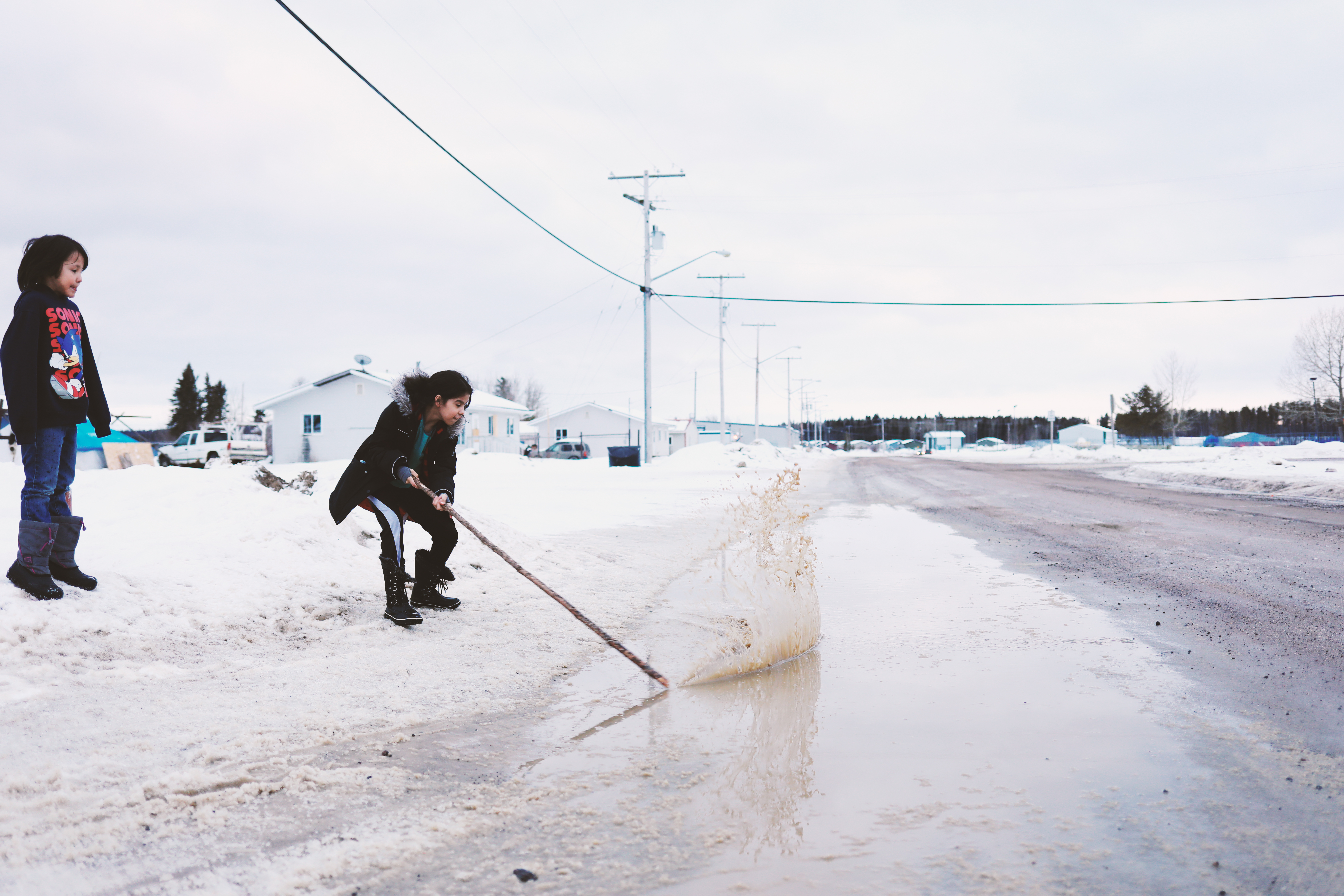 Children hit water with a stick for fun in Stanley Mission on March 7, 2020. (Heidi Atter/CBC)