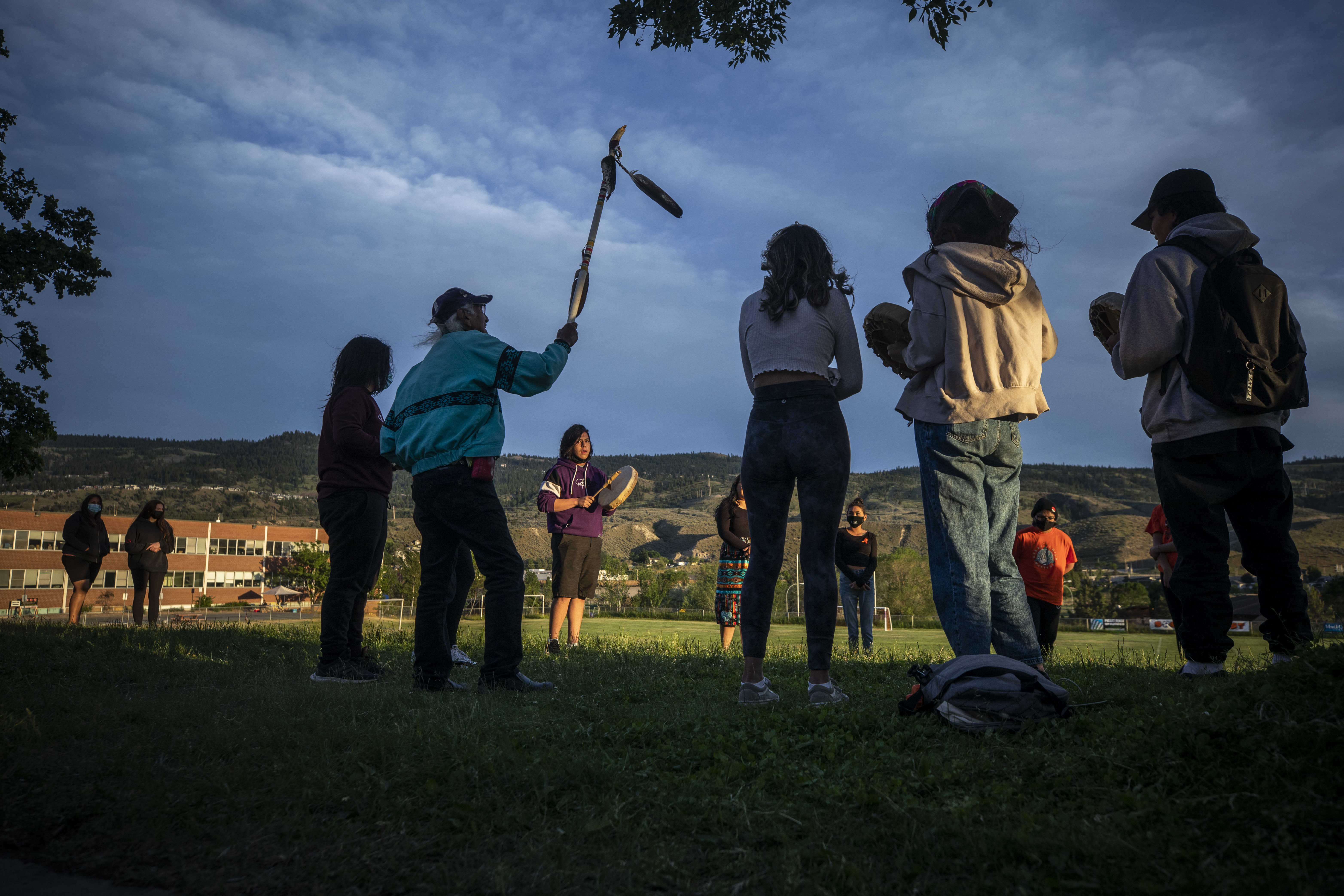 Kamloops Indian Residential School survivor Stanley Paul, 75, who was forced into the school at the age of seven, holds a walking stick in the air while Cash Charters sings and drums with a group of youths at a monument outside the former school.