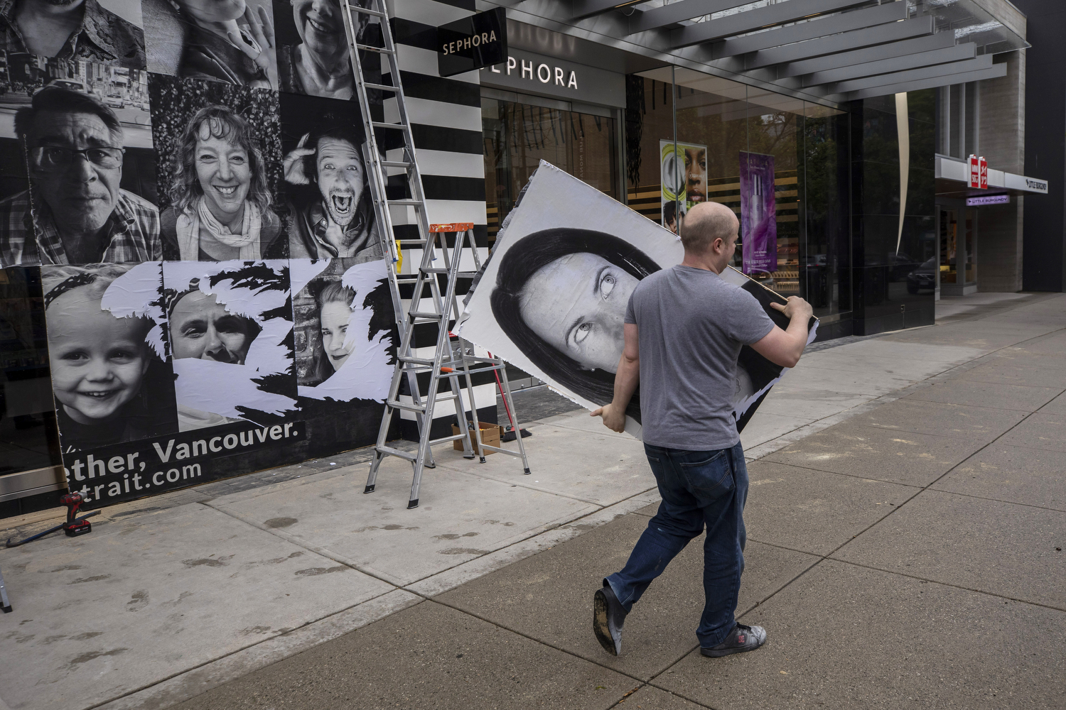 Workers take down plywood boards painted with murals covering up entrances of stores on Vancouver's Robson Street on May 11, 2020. B.C. entered Phase 2 of its pandemic restart program on May 19, allowing stores to reopen. (Ben Nelms/CBC Vancouver)