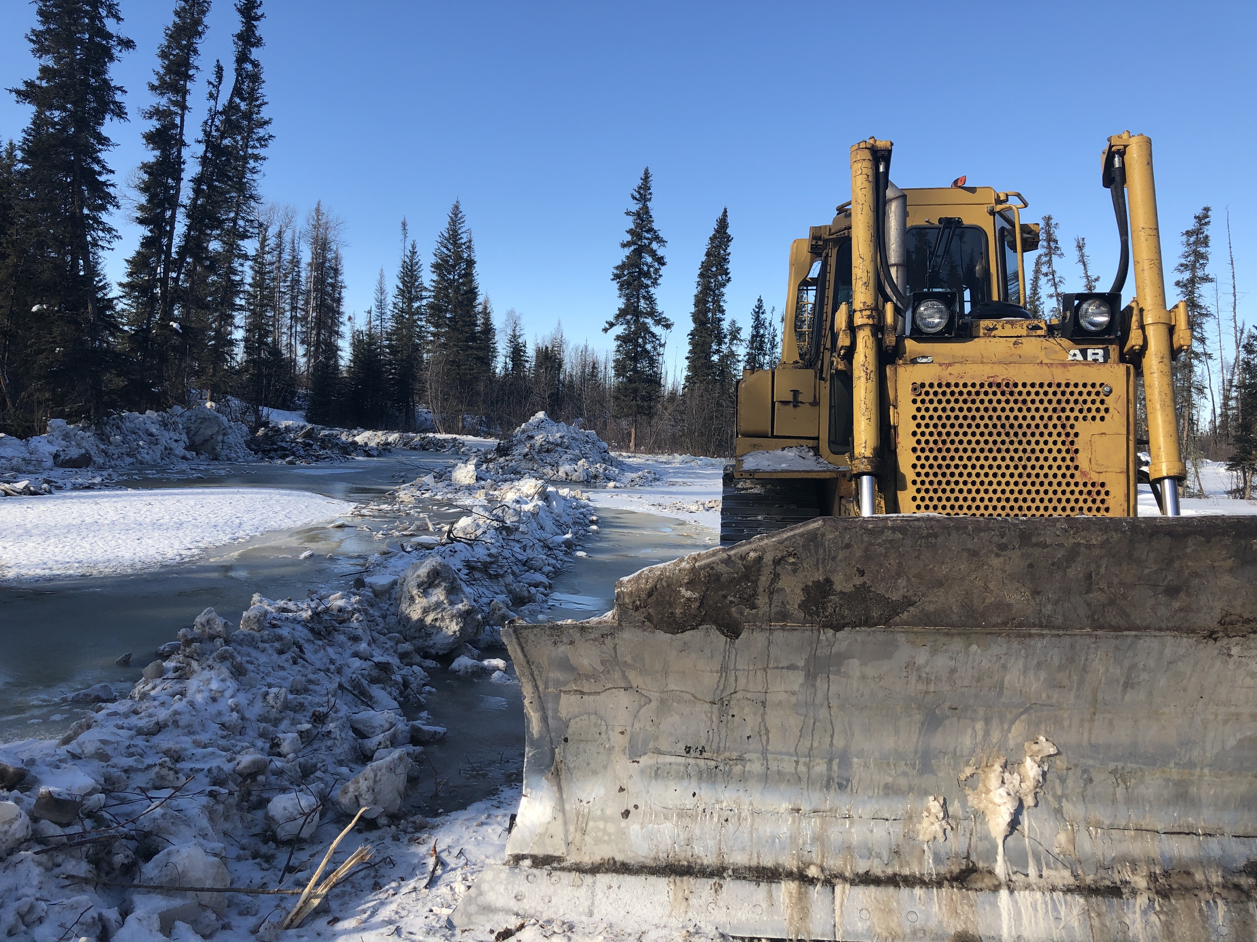 'Precious,' a 20-year-old grader owned by the Department of Infrastructure, at an overflow zone north of Wrigley. Overflow results when melt water breaks through snow and ice and covers the road, turning it to slush. (John Last/CBC)