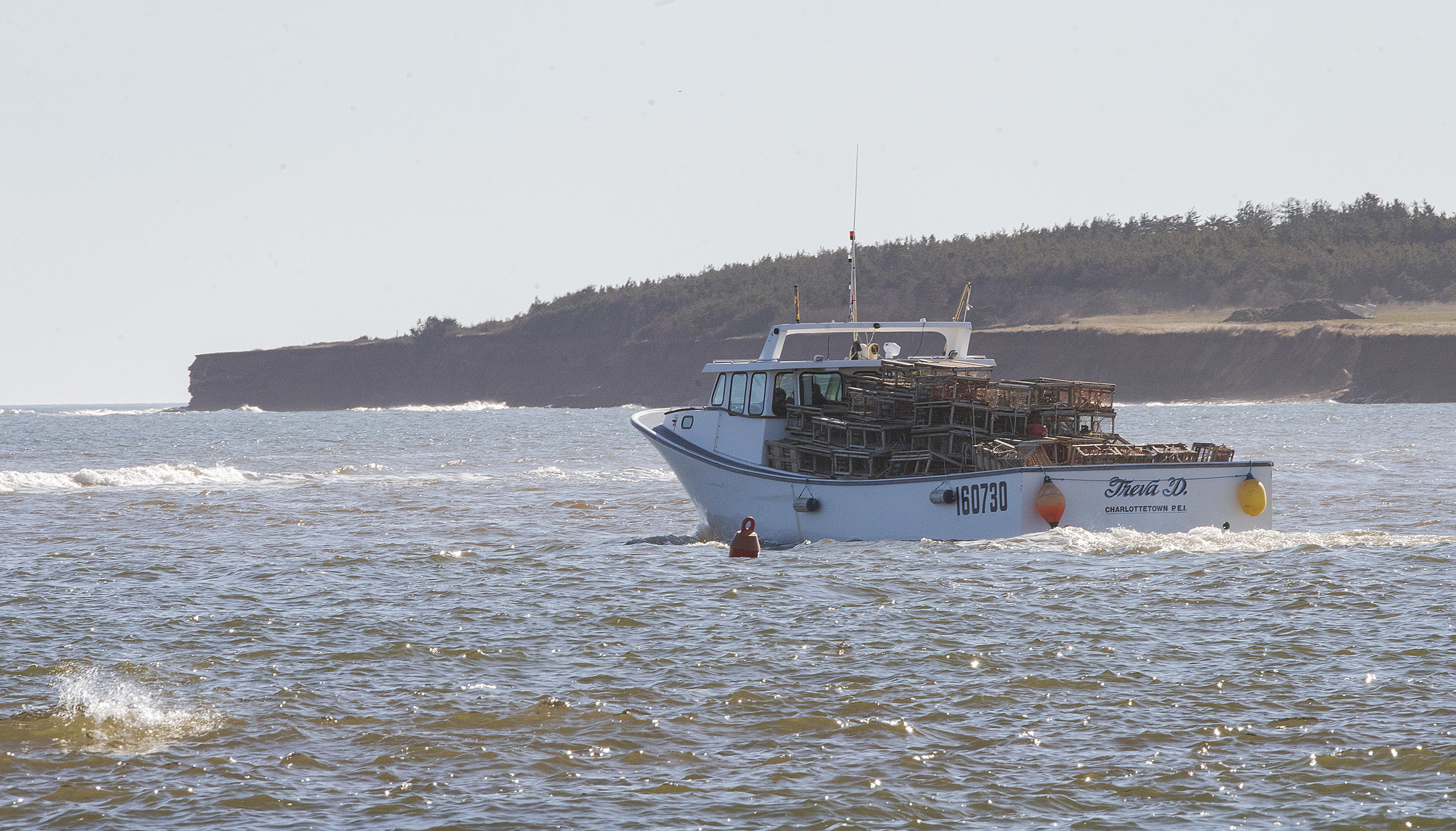 A lobster boat sails past the red sandstone cliffs bordering Malpeque Harbour as it heads out into the Gulf of St. Lawrence on the opening day of the lobster season. (Brian McInnis/CBC)