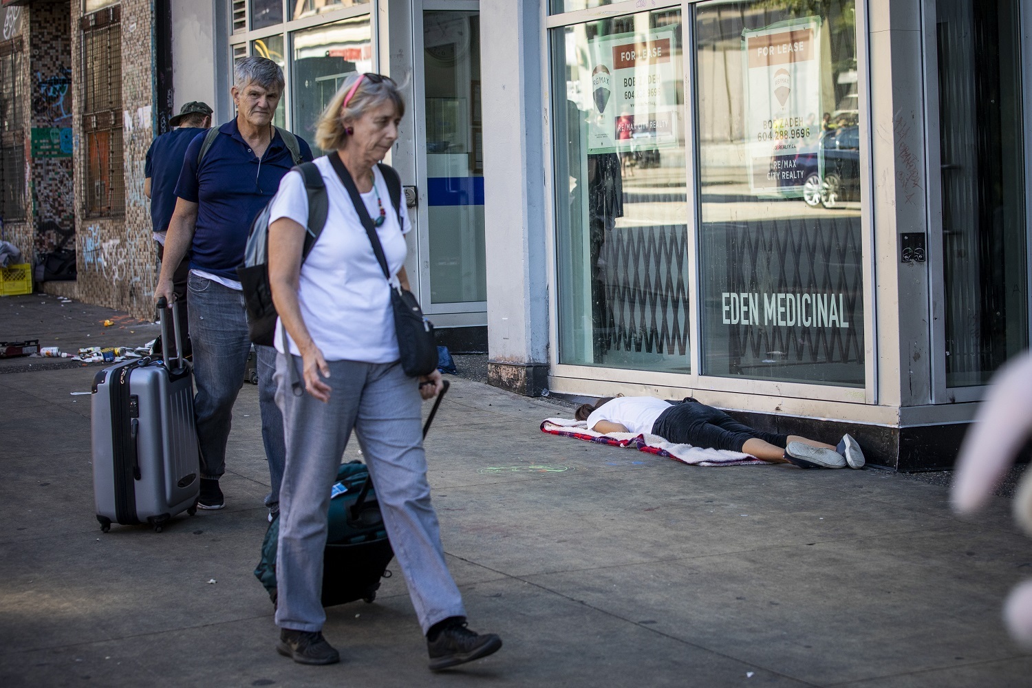 A man and woman walk past a woman lying on the ground along Hastings Street in Vancouver, British Columbia on Friday, September 6, 2019. (Ben Nelms/CBC)