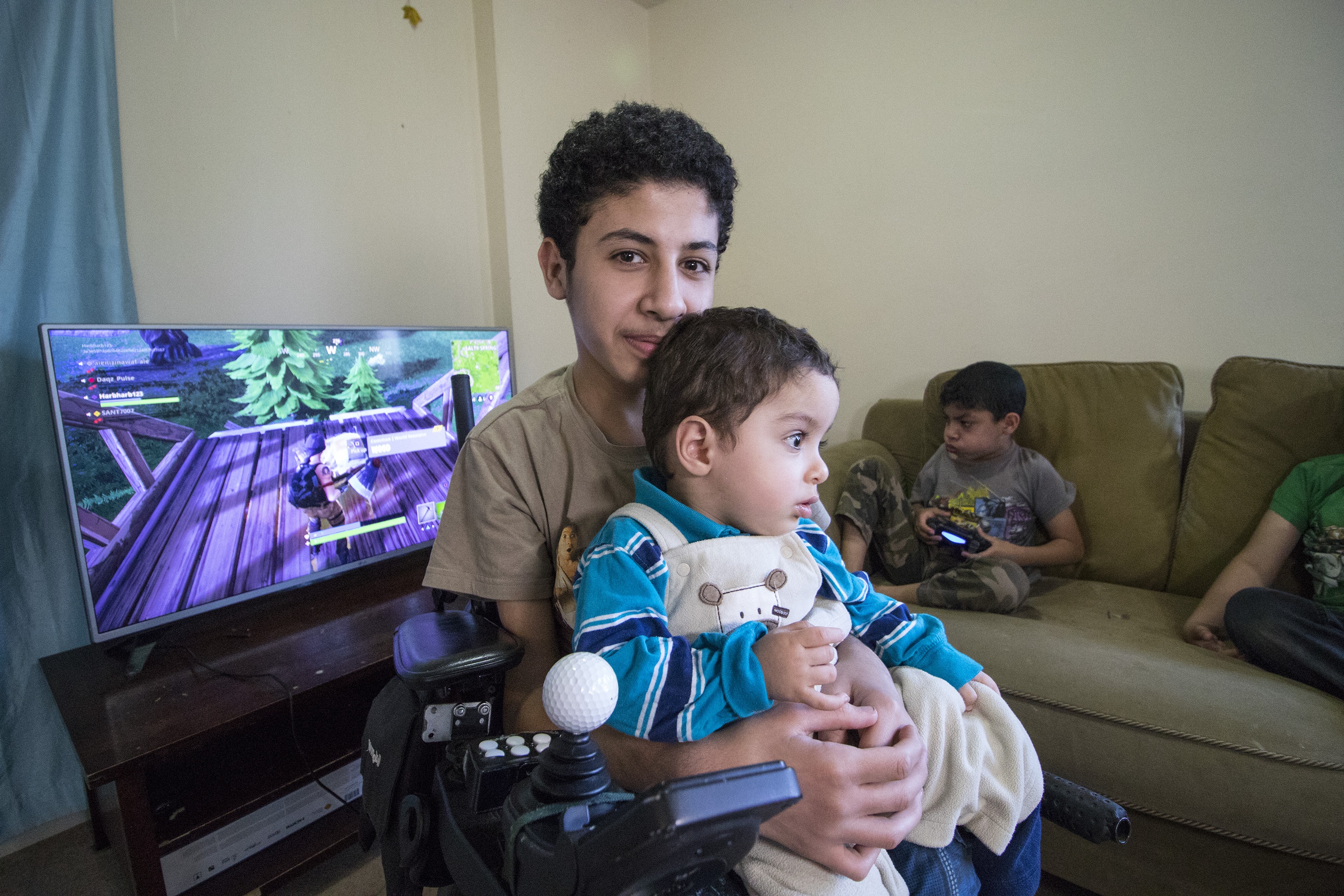 Maher holds Mias, who has also been diagnosed with muscular dystrophy. Younes is playing video games. (Dave Irish/CBC)