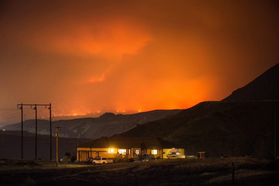 A wildfire burns on a mountain in the distance east of Cache Creek behind a house in Boston Flats, B.C. on Monday July 10, 2017.