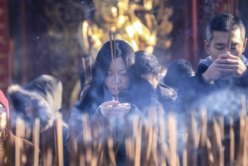 A woman prays while holding incense sticks between her hands. (Tina Lovgreen/CBC)