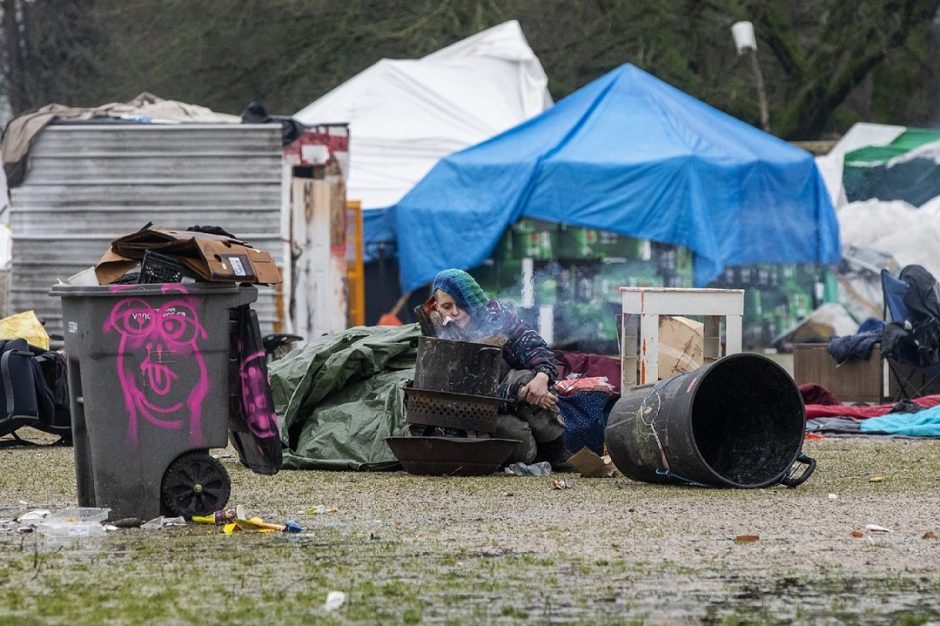 A woman sits by a small fire trying to keep warm in front of a collection of makeshift shelters and tents. (Ben Nelms)