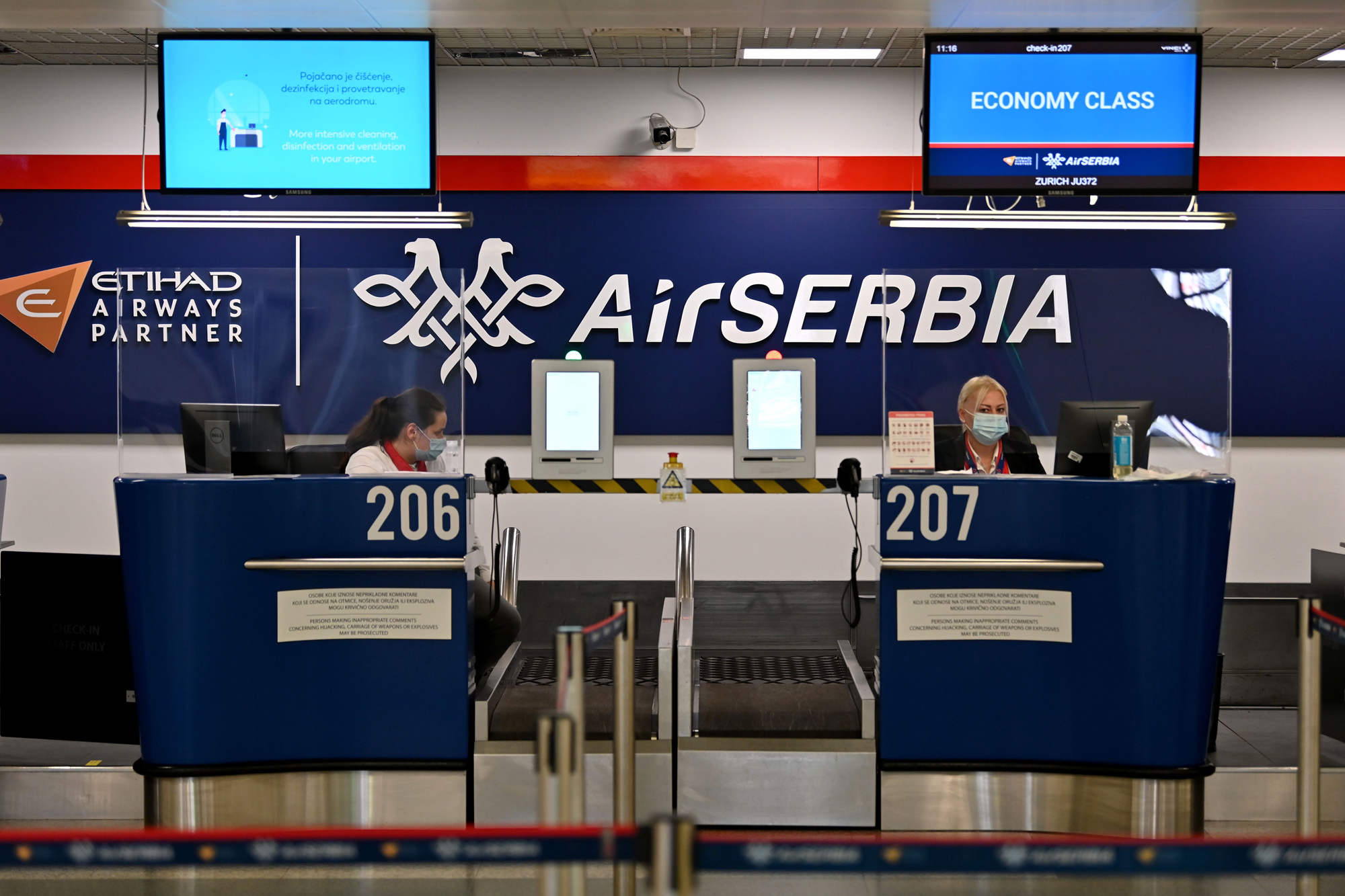 Airport personnel wait for passengers behind Plexiglas at the check-in counters at Belgrade's airport. (Andrej Isakovic/AFP via Getty Images)