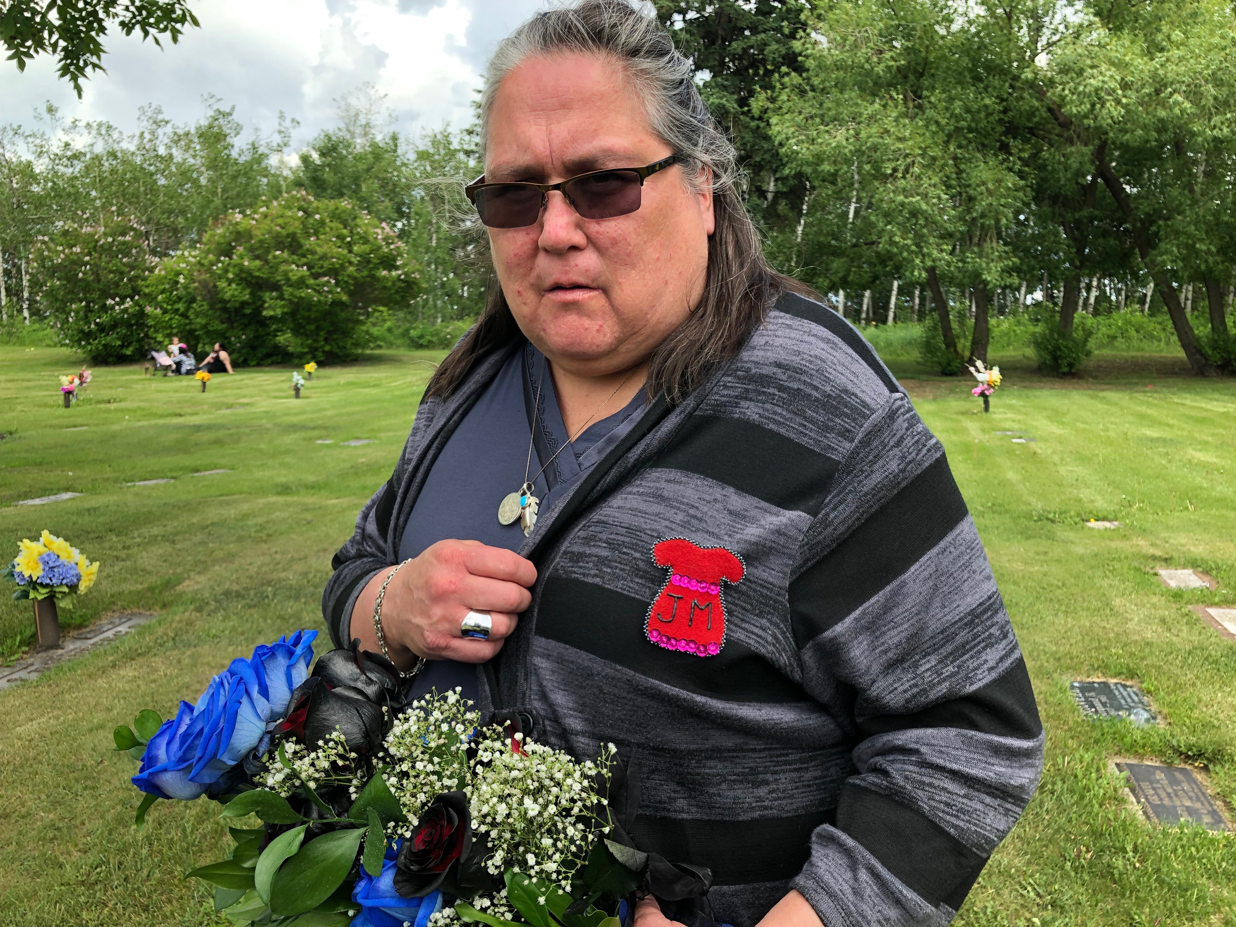 Betty Bird at the Edmonton graveyard where her friend is buried. Bird is wearing a red dress pin, a symbol for missing and murdered Indigenous women, with Mercredi's initials. (Rachel Zelniker/CBC)