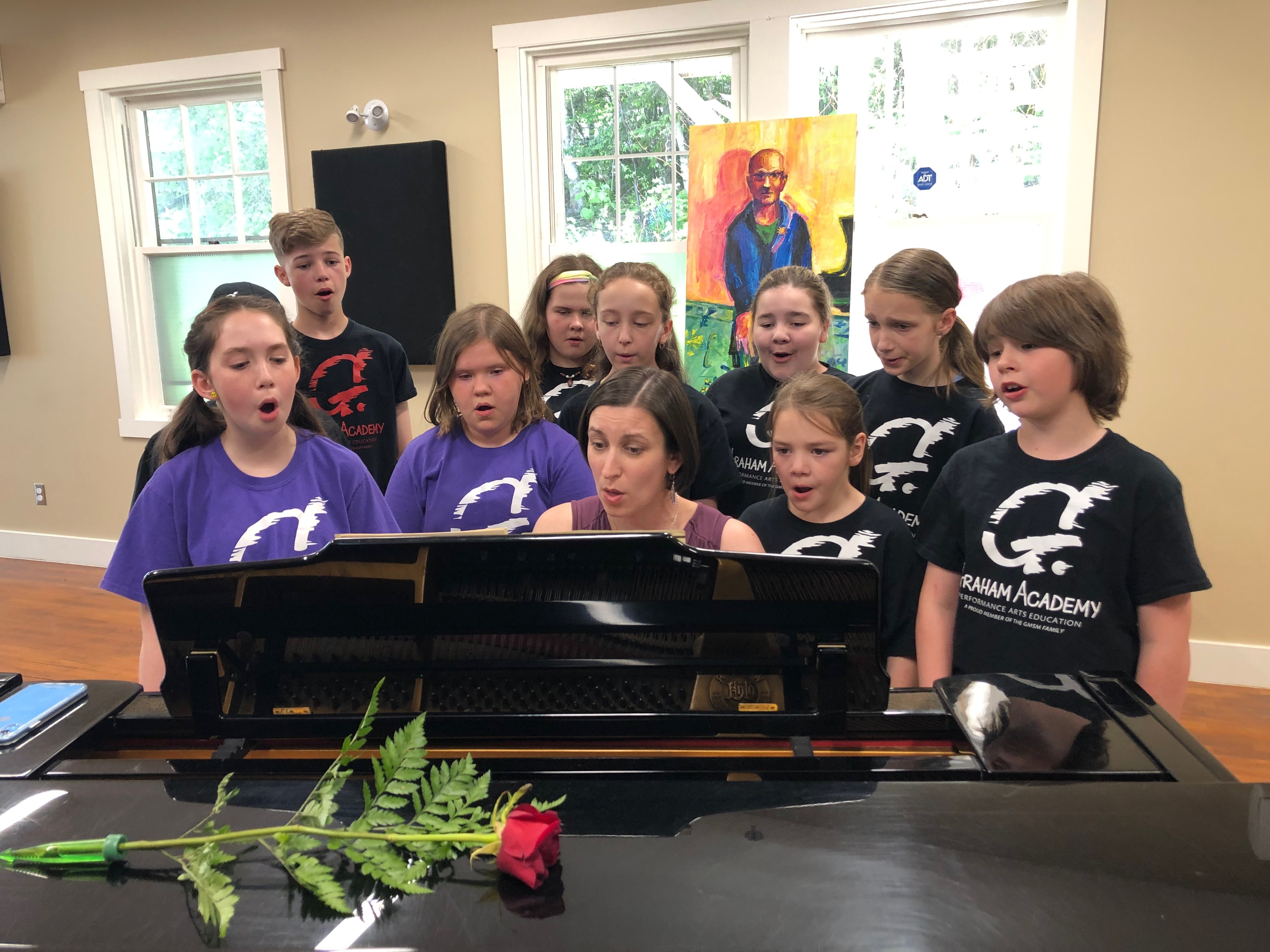 Students of the Graham Academy sing a song with choral instructor Jennifer Stratton-Renouf, as the memorial portrait of Gary Graham hangs in the background. (Jen White/CBC)