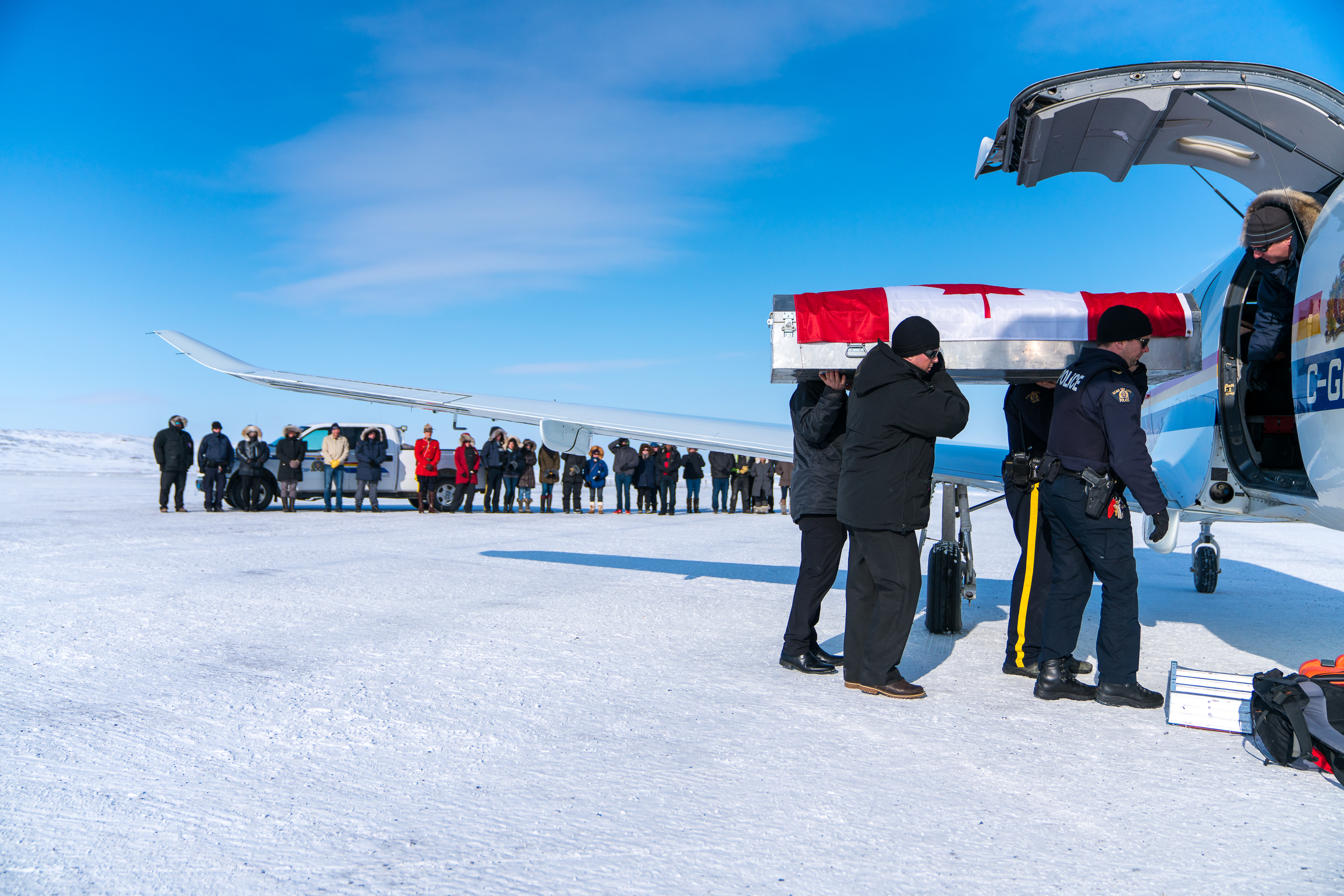 Community members watch as the body of Cst. Graham Holmes is loaded into an airplane in Kugluktuk, Nunavut. The 30-year-old died when his snowmobile went over a cliff in April 2018 (DnV Photo)