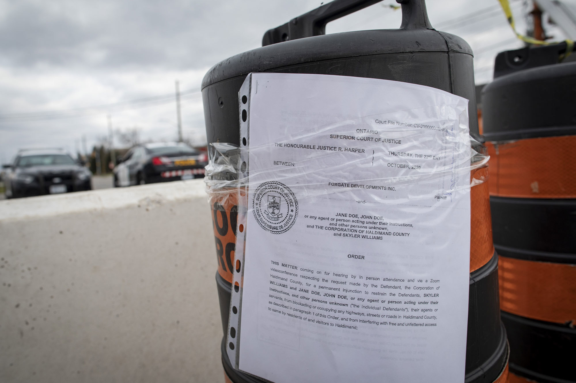 Top, a school bus acts as a barricade on Argyle Street South. Below, a copy of the injunction issued by Ontario Superior Court to halt the occupation of McKenzie Meadows is affixed to a pylon on Argyle. (Evan Mitsui/CBC)