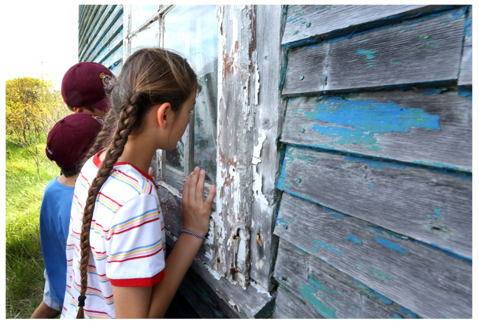 Left-Right: Beatrix Potter Elementary students Oscar Heard, Sasha Cellino and Sophia Anderson look through the window of the abandoned home of Silas Edgecombe in Ochre Pit Cove. Photo by Paul Daly for CBC