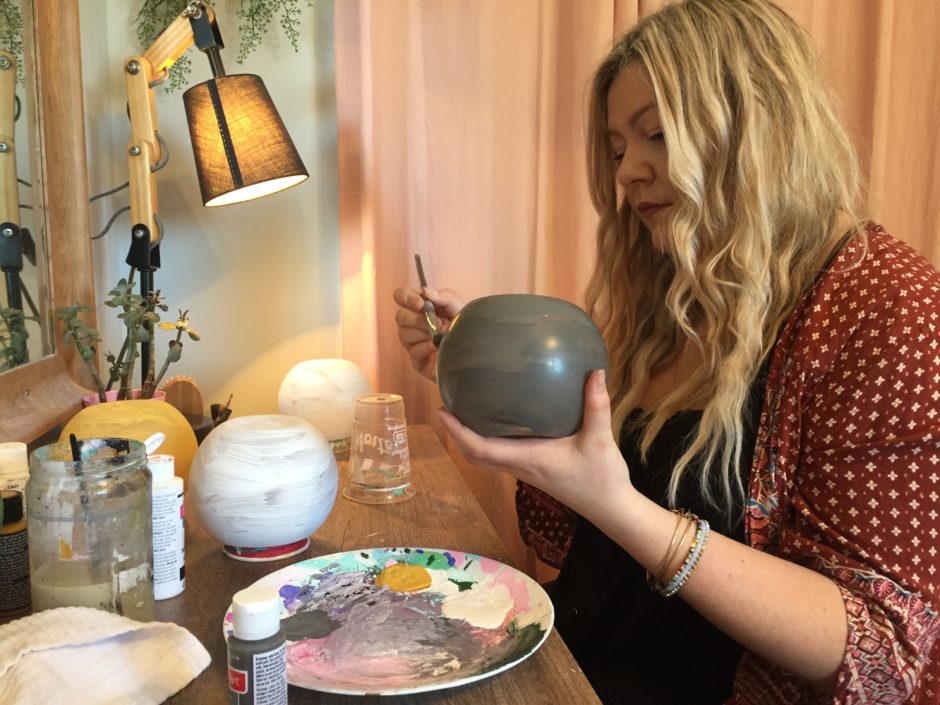 Shila Pennell sits at her paint station, which also serves as her bedroom vanity table, painting flower pots to sell on her Instagram business account. (Stephanie Tobin/CBC)