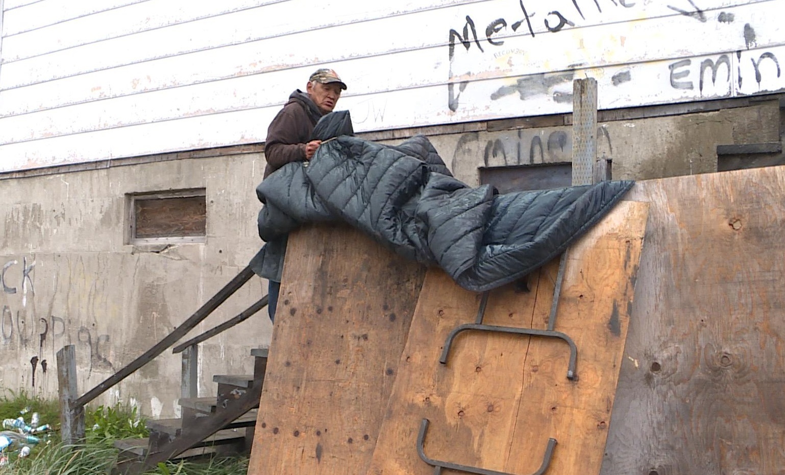 Abele Ikkusek adjusts the shelter he's built on the porch of the old council hall. (Jacob Barker/CBC)