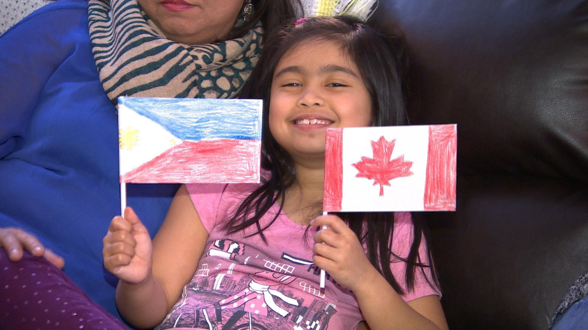 Lexie holds up two handmade flags — one for Canada and one for the Philippines. She said her dad helped her draw the maple leaf. (Travis Golby/CBC)