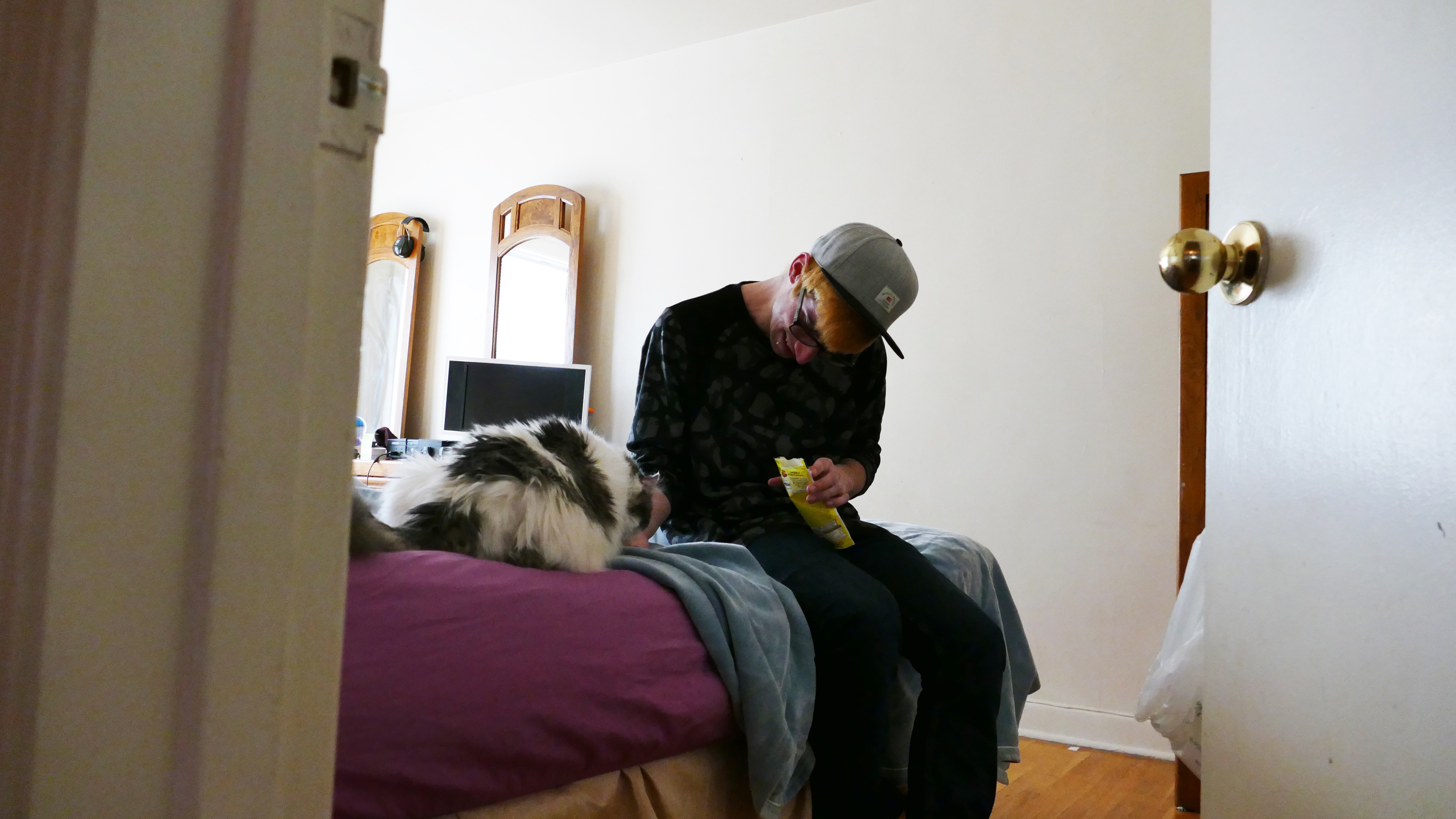 Lavallee feeds his cat some treats while the two sit on a bed in his apartment. (Warren Kay/CBC)