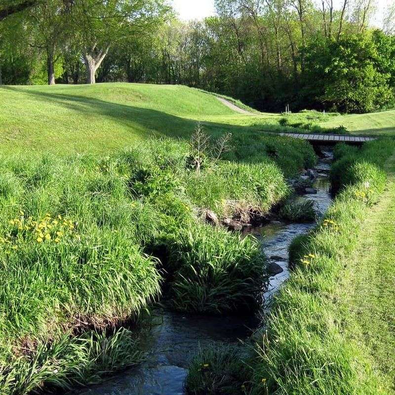 A creek flows past mowed green lawns.