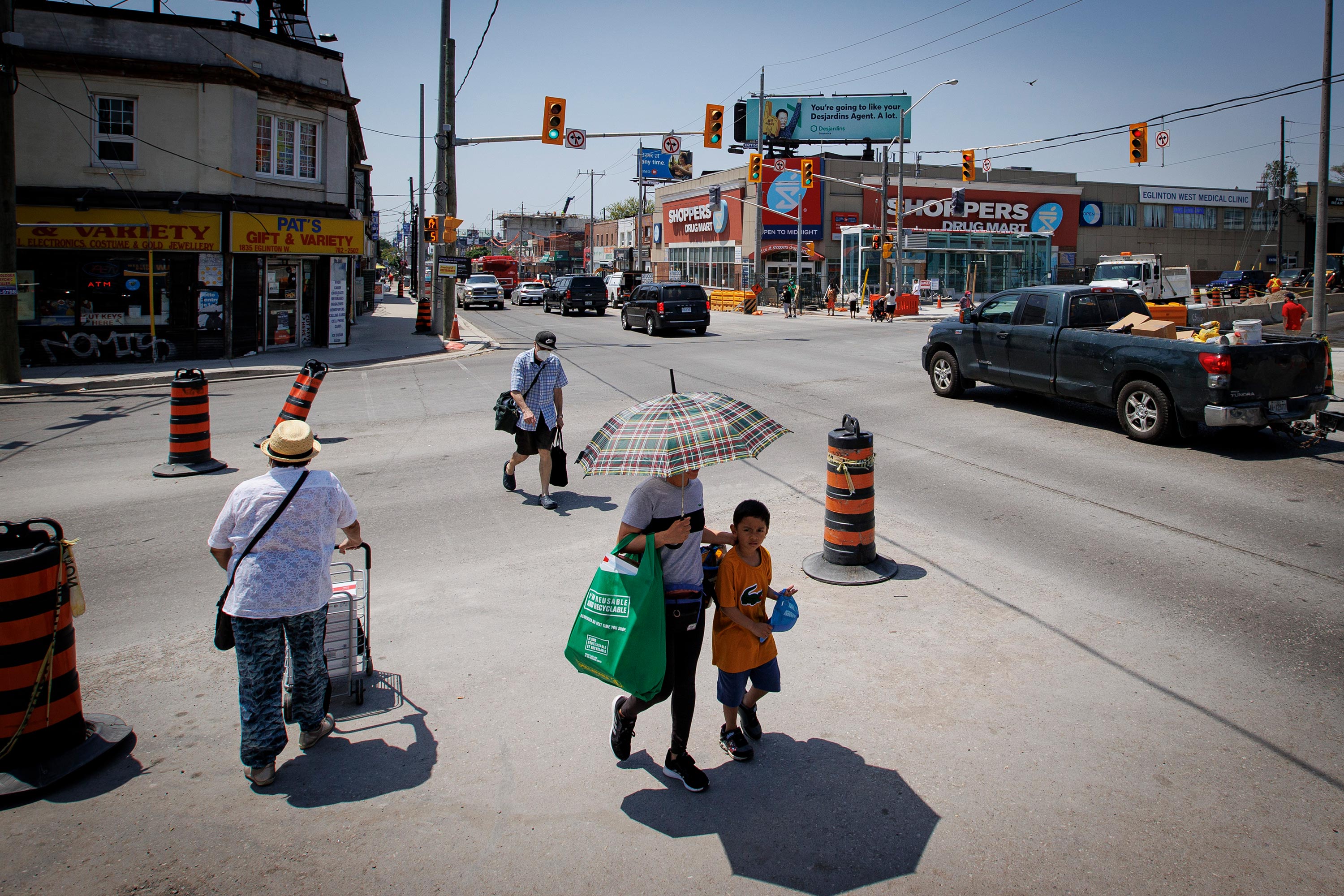 Pedestrians use an umbrella to shield themselves from the sun’s rays as they cross the intersection of Eglinton and Dufferin in Toronto on May 30, 2022