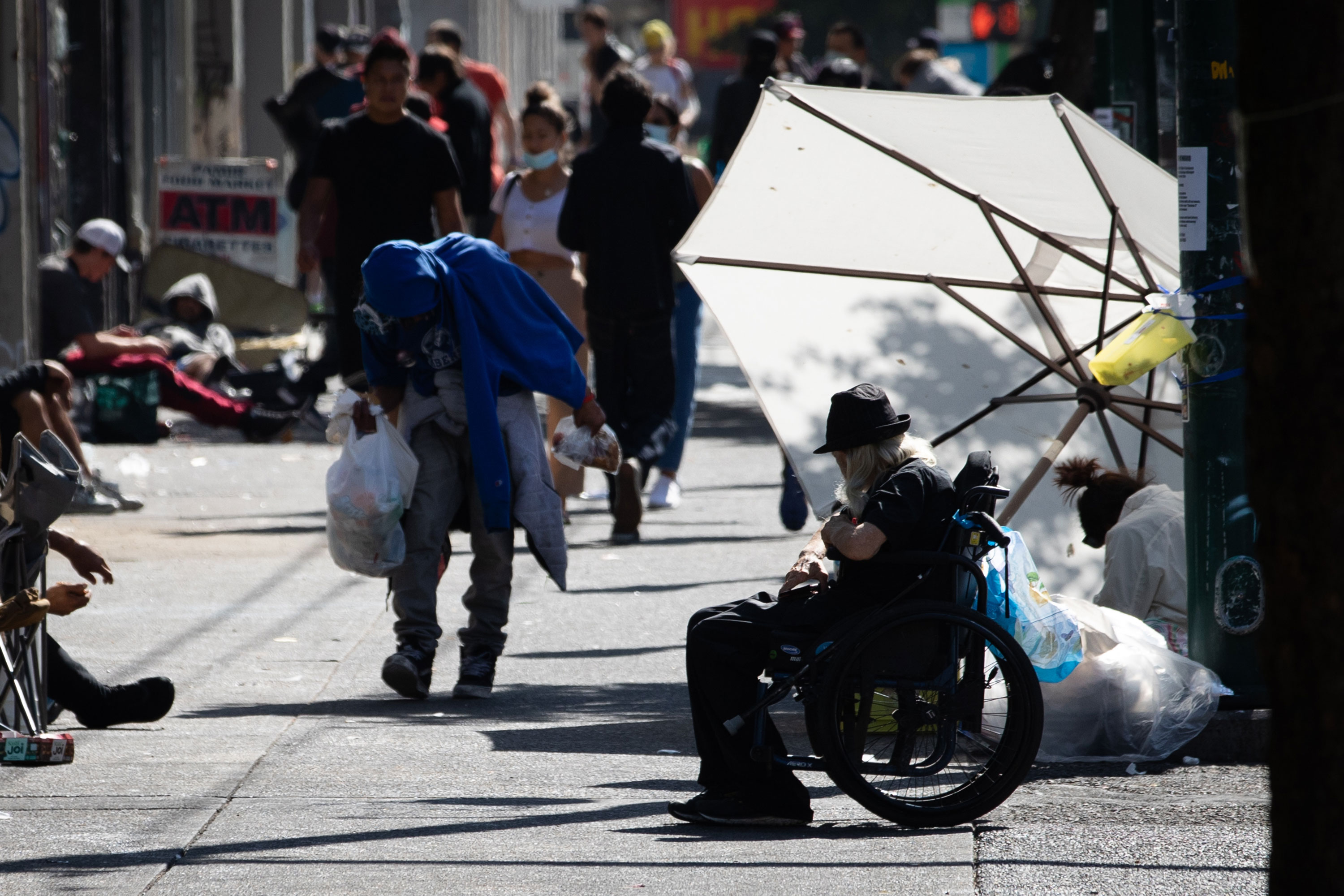 A large umbrella blocks the sun for a woman sitting on the sidewalk in Vancouver’s Downtown Eastside in July 2021.