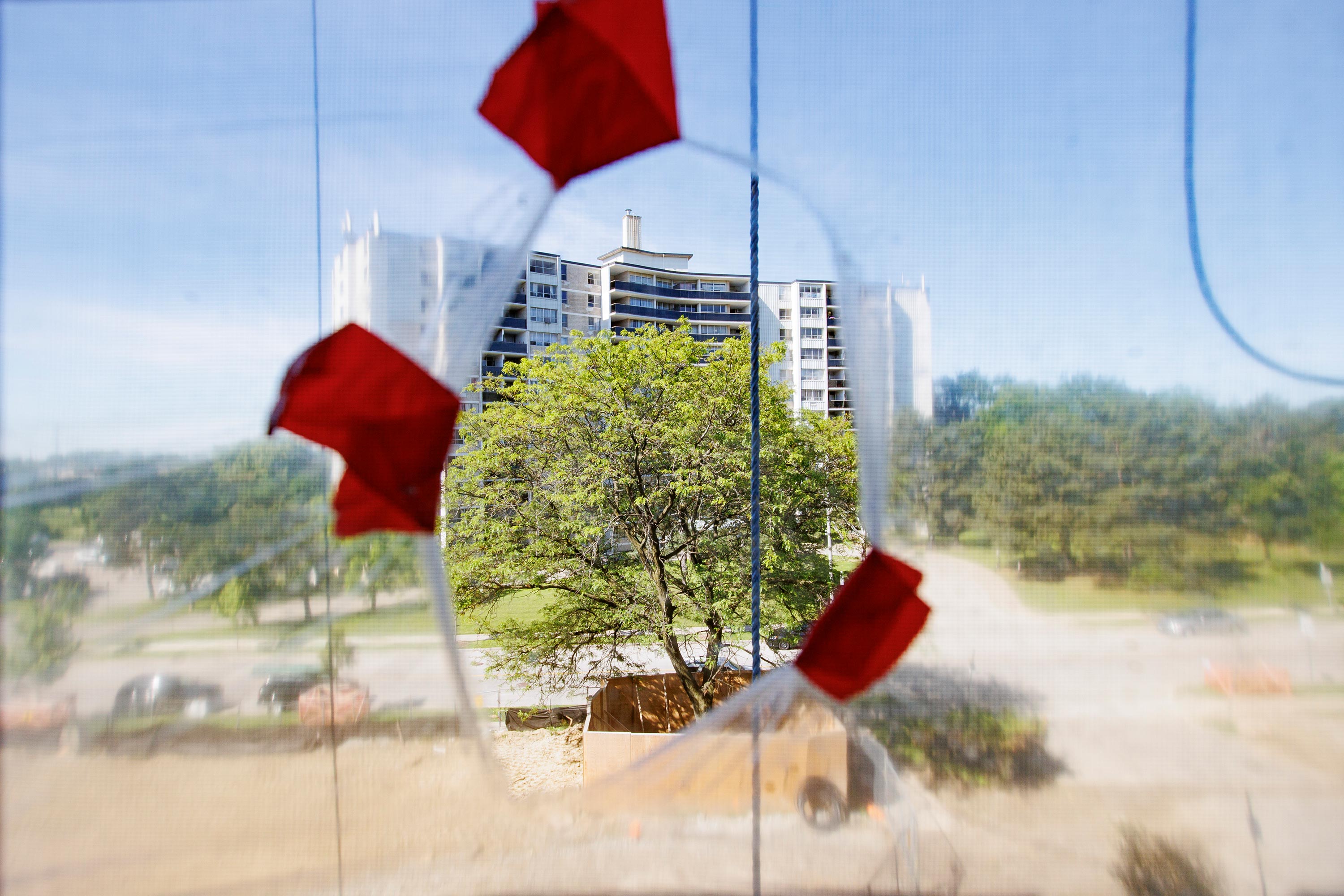 Bojana Nakic, pictured on June 13, 2022, looks out her bedroom apartment window. A hole was made in protective plastic coating taped over her window to allow some fresh air to circulate as construction progresses on the building.