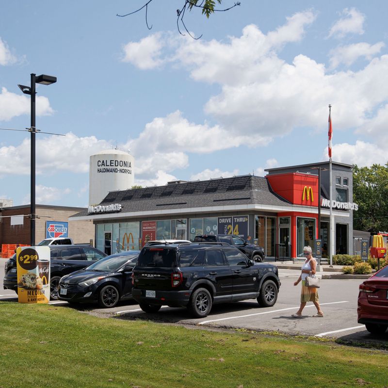 In the distance, a white tower is marked “Caledonia: Haldimand-Norfolk”. In the foreground, a woman walks through a McDonald’s parking lot in an urban setting.