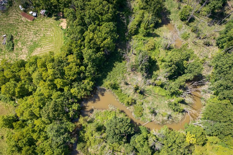 An aerial top-down view shows a small brown creek winding through wooded rural land.